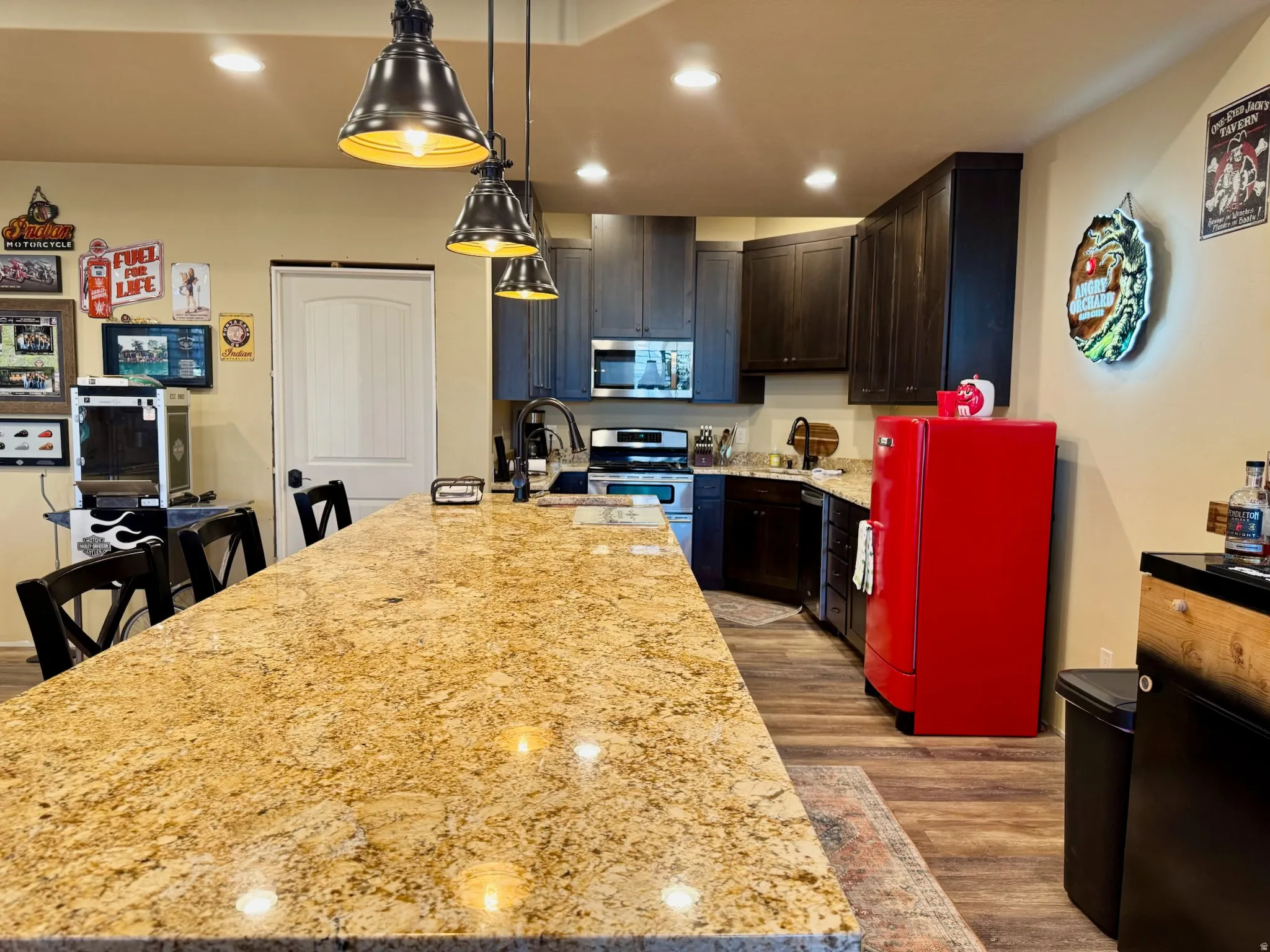 Kitchen featuring light wood-style floors, light stone counters, stainless steel appliances, pendant lighting, and a kitchen island with sink
