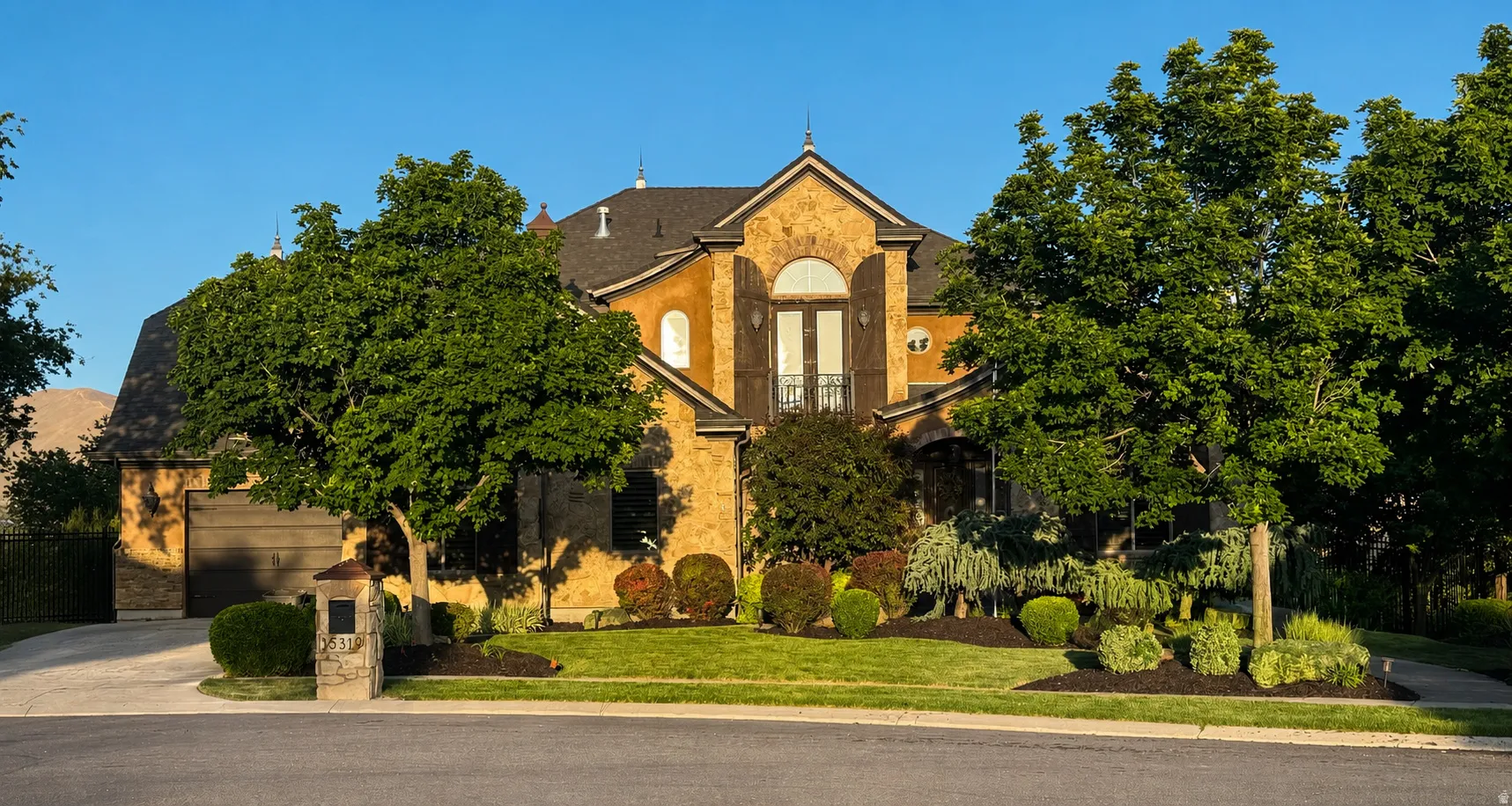 Stately stone and stucco residence featuring a prominent arched window with wrought iron detailing, a two-car garage, and a concrete driveway