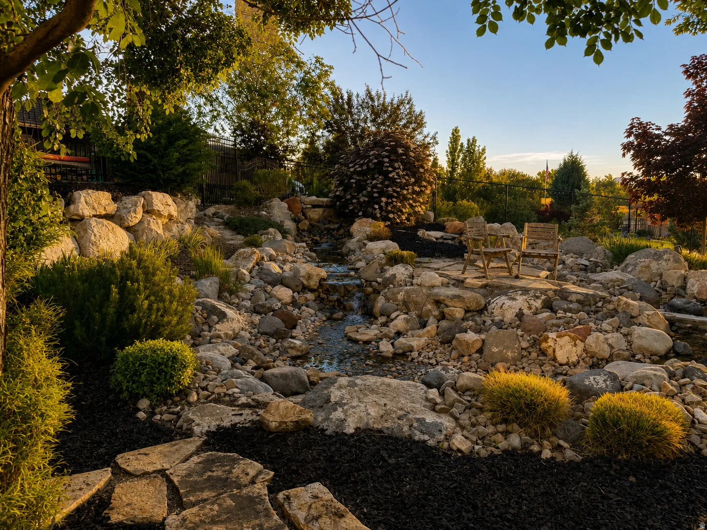 Rock garden with integrated water feature, featuring natural stone landscaping, varied evergreen and deciduous plantings, and a flagstone pathway