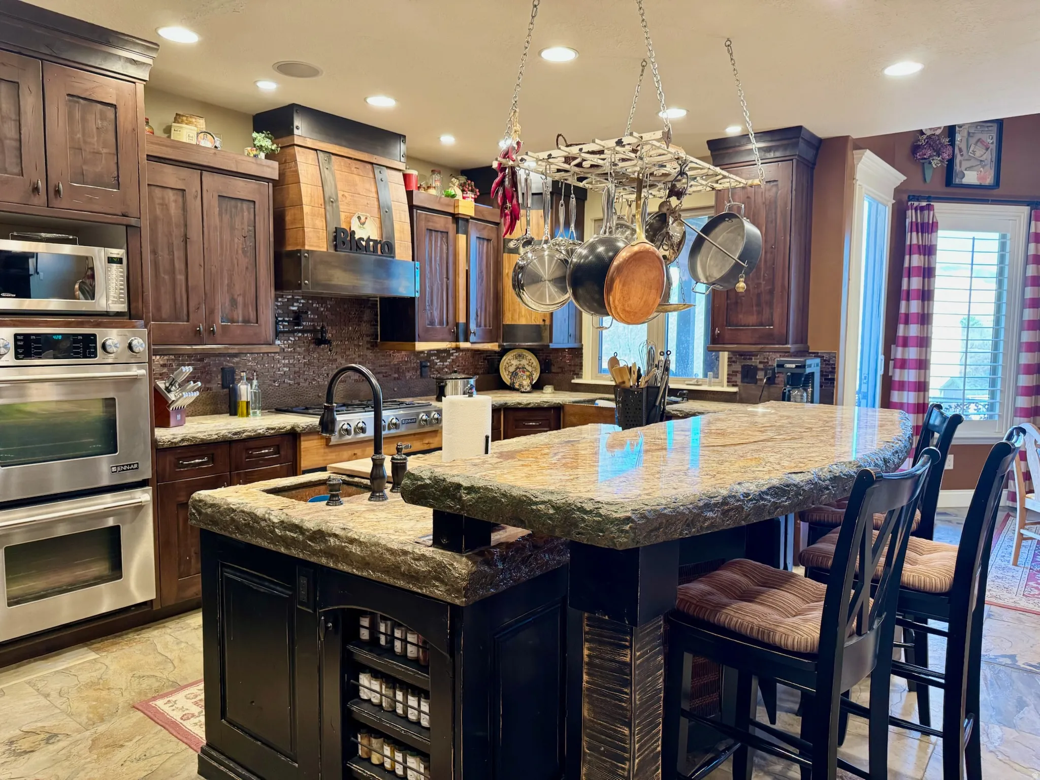 Dual tone kitchen featuring stainless steel appliances, dark stone countertops, a center island with sink, a breakfast bar area, and recessed lighting