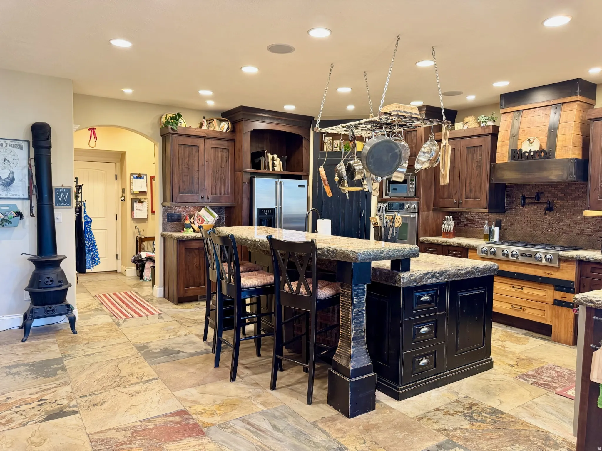 Two tone kitchen featuring arched walkways, a center island with sink, a breakfast bar area, dark stone counters, and stainless steel appliances
