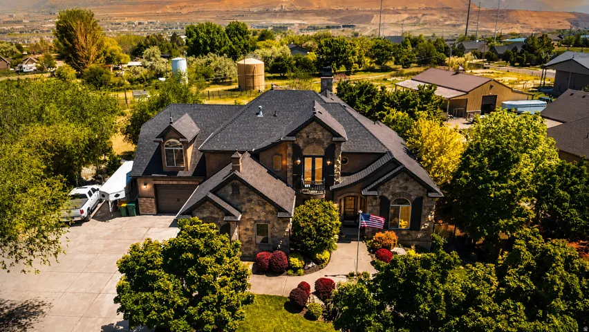 Stone and stucco exterior residence featuring a multi-gabled roof, arched entryways, a paved driveway, and mature landscaping