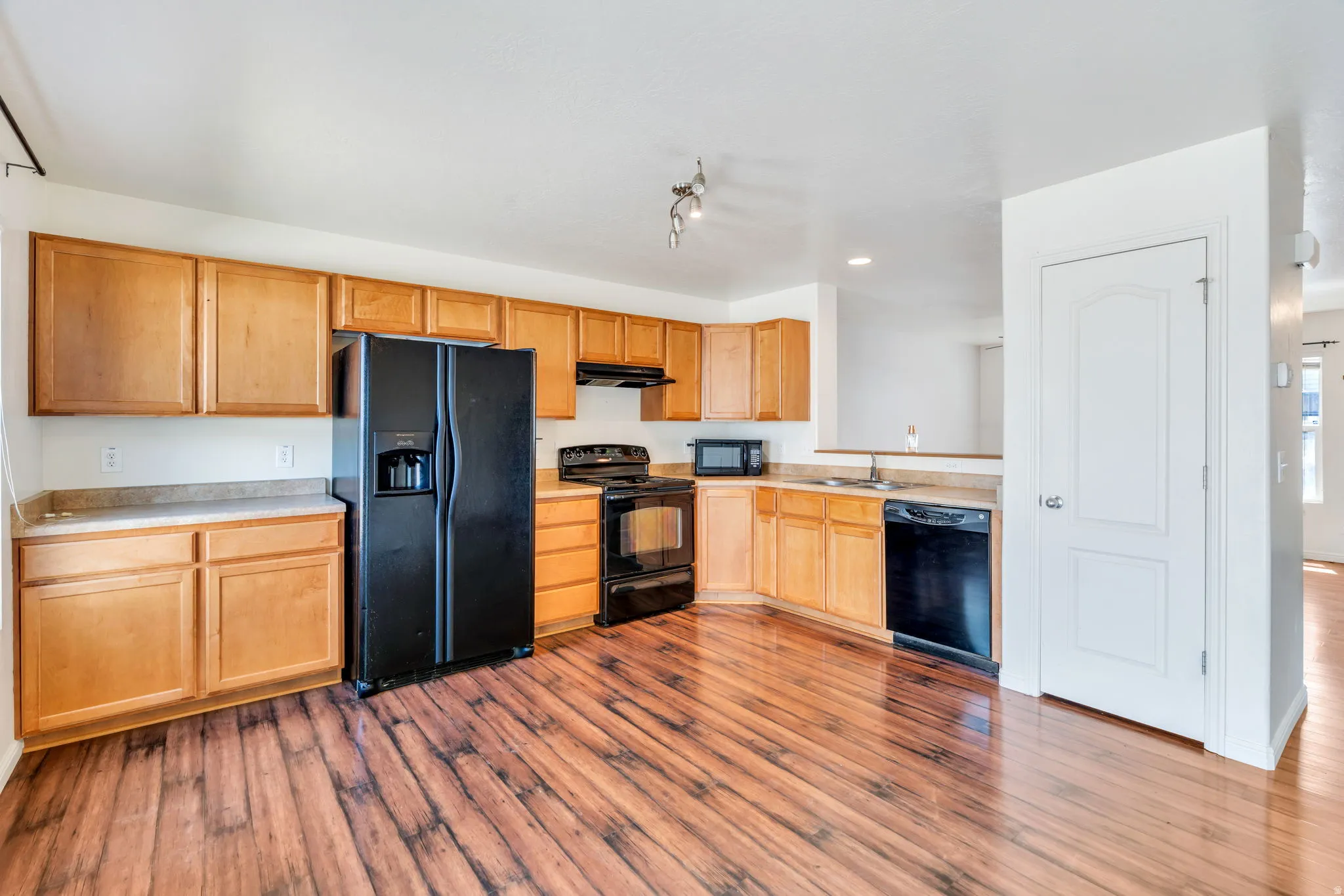 Kitchen featuring abundant light wood cabinetry, dark wood-finish flooring, black appliances, track lighting, and a neutral countertop