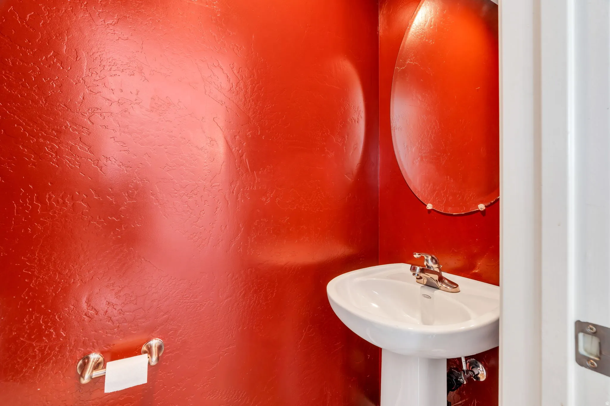 Powder room with a pedestal sink, chrome faucet, and an oval mirror