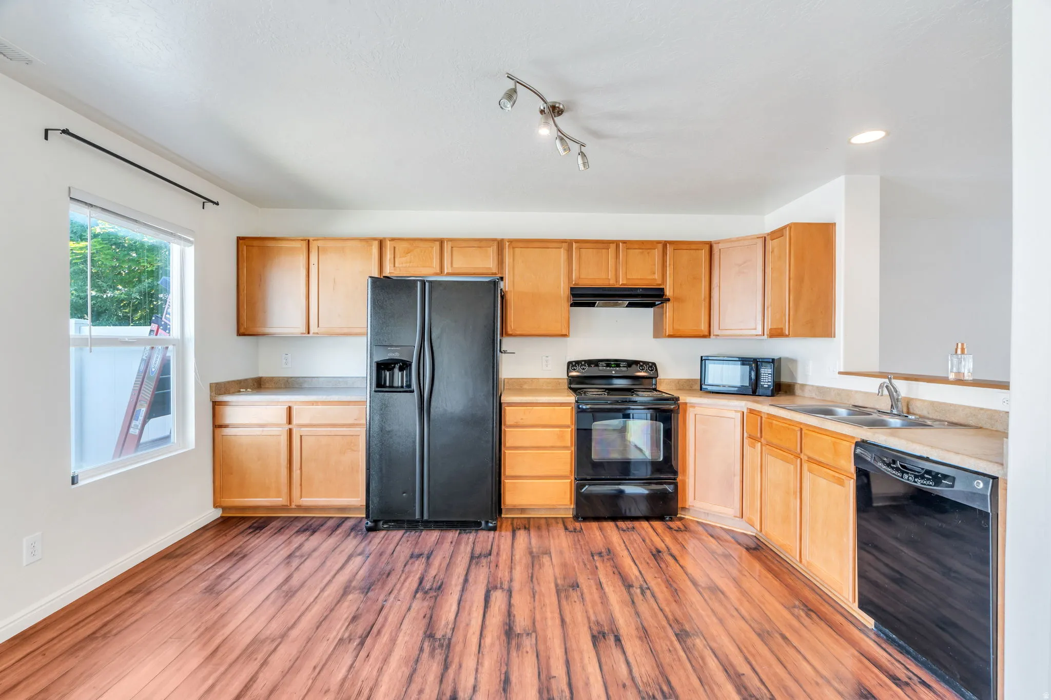 Kitchen featuring wood-finish flooring, light wood cabinetry, black appliances, track lighting, and a stainless steel double basin sink