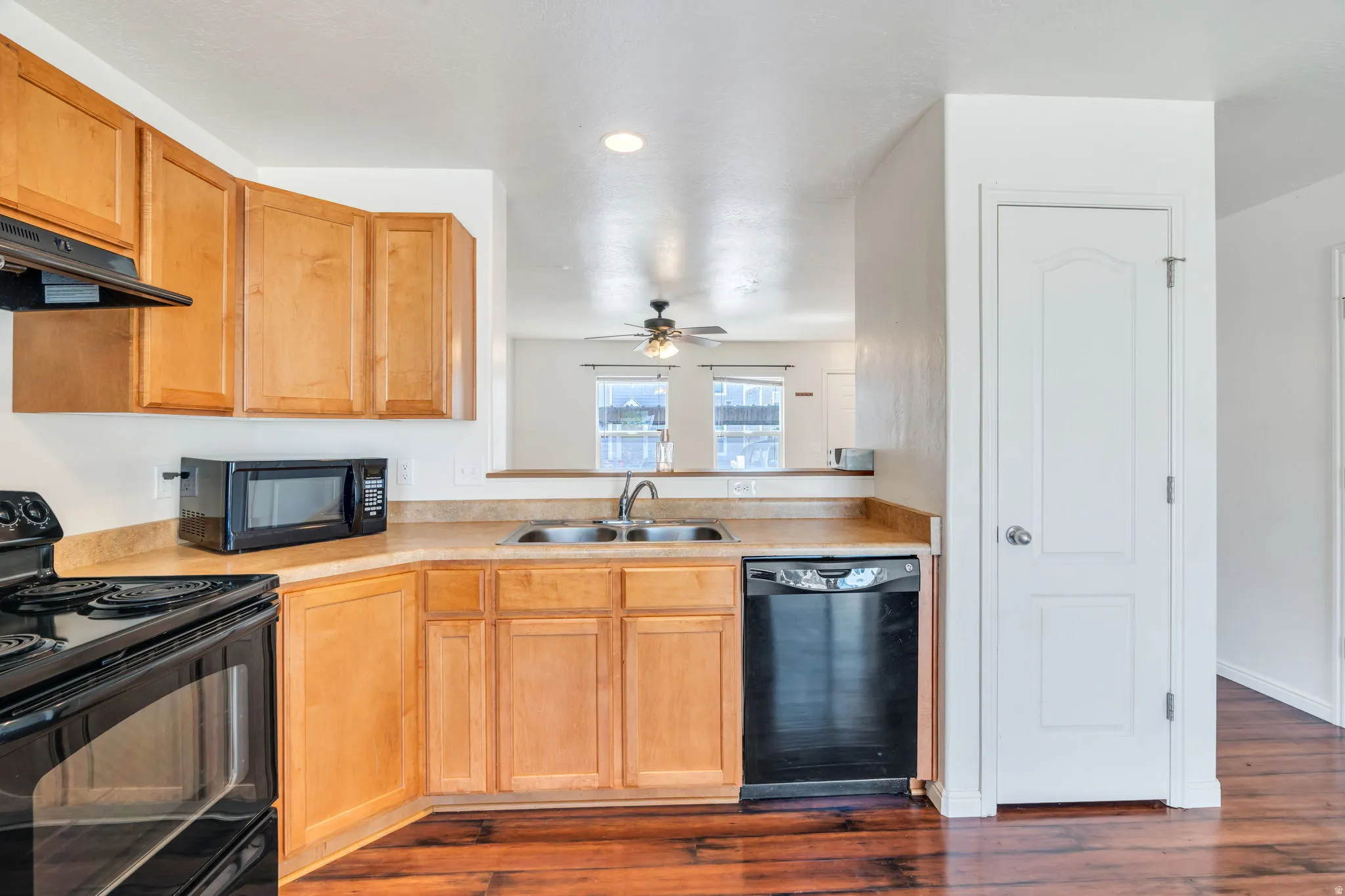 Kitchen featuring wood-finish flooring, light wood cabinetry, laminate countertops, and a black appliance suite including a dishwasher and range