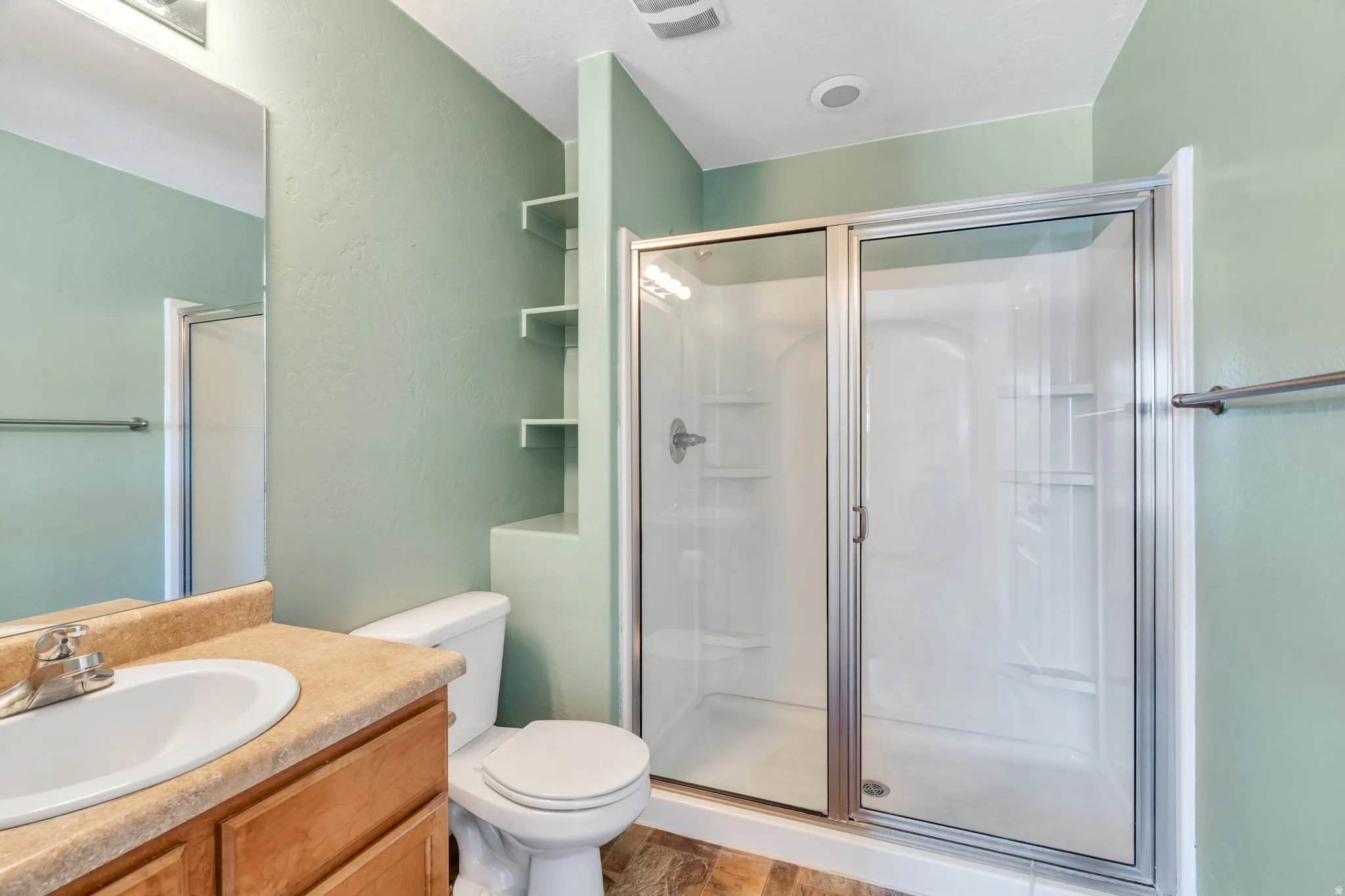 Bathroom in south bedroom featuring a glass-enclosed shower, built-in shelving, wood-finish vanity, integrated sink, and vanity mirror