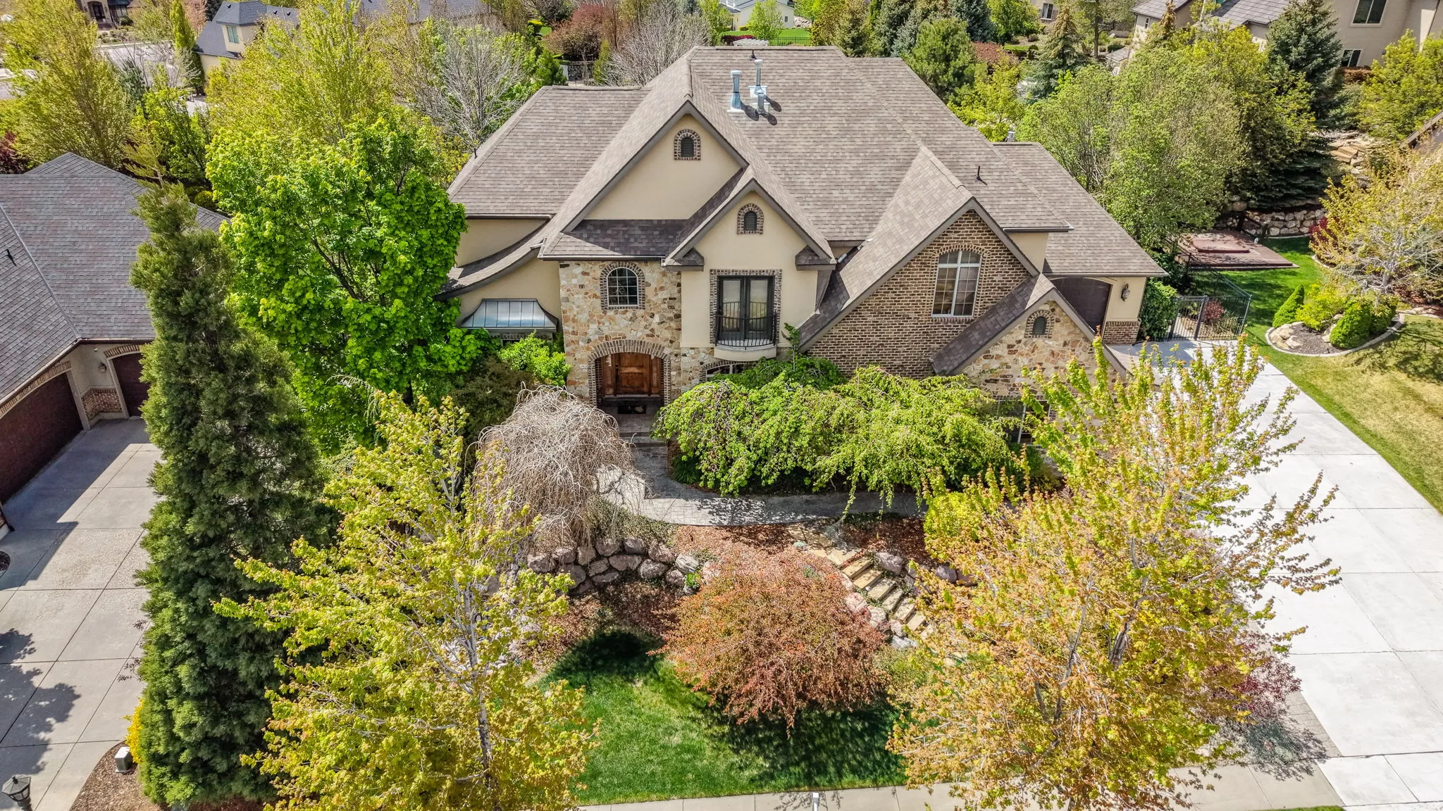 View of front of house featuring stucco siding, a shingled roof, stone siding, and view of scattered trees