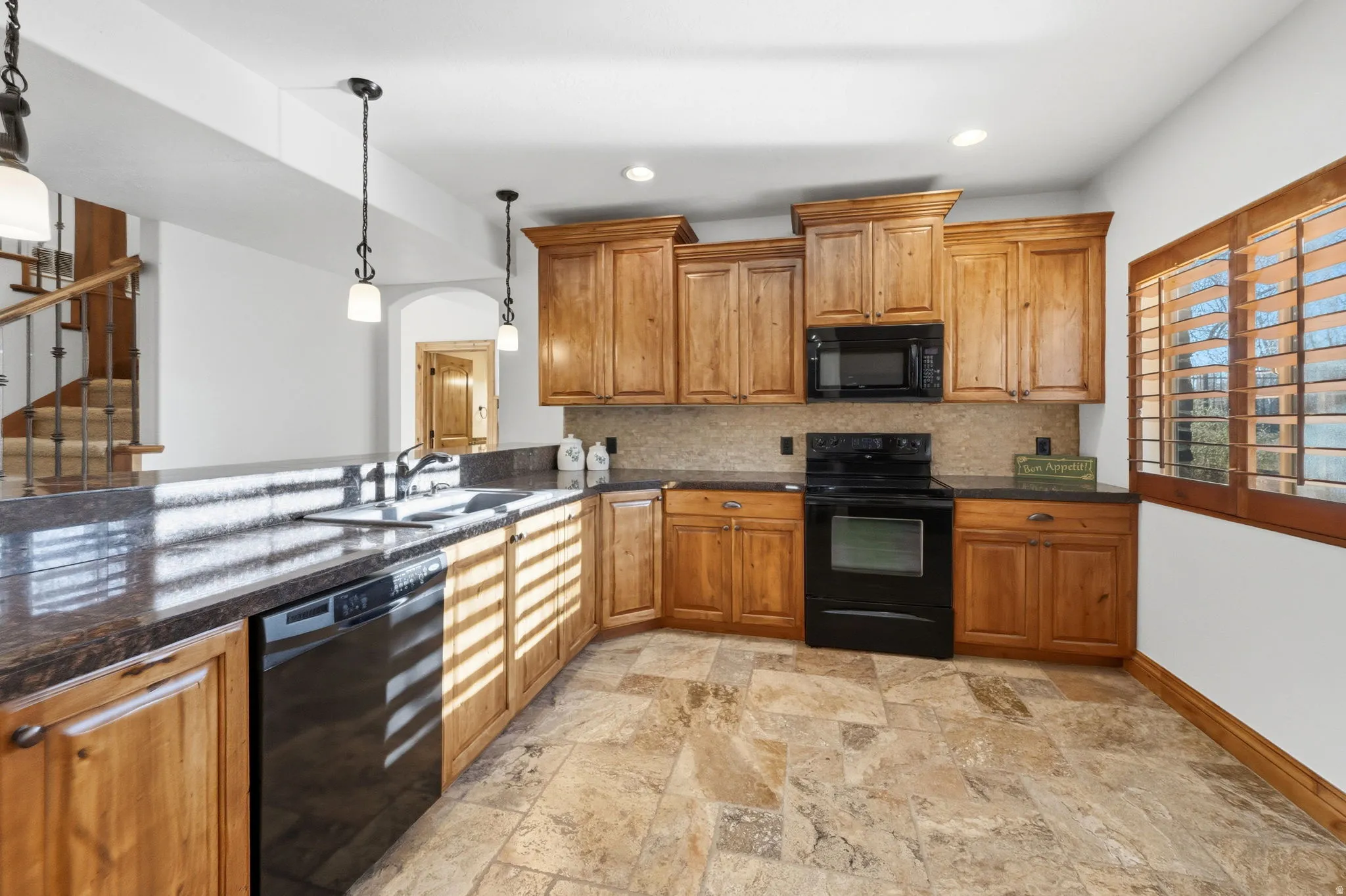 Kitchen featuring black appliances, wood finish cabinetry, hanging light fixtures, and backsplash
