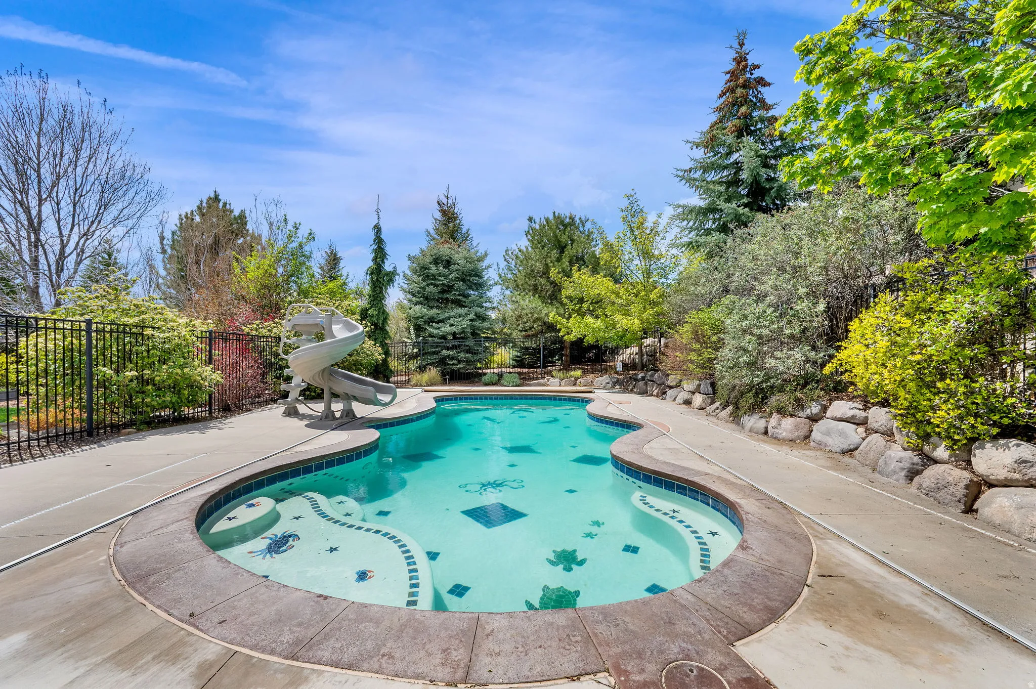 View of pool featuring patio surround, a fenced backyard, a water slide, and view of wooded area