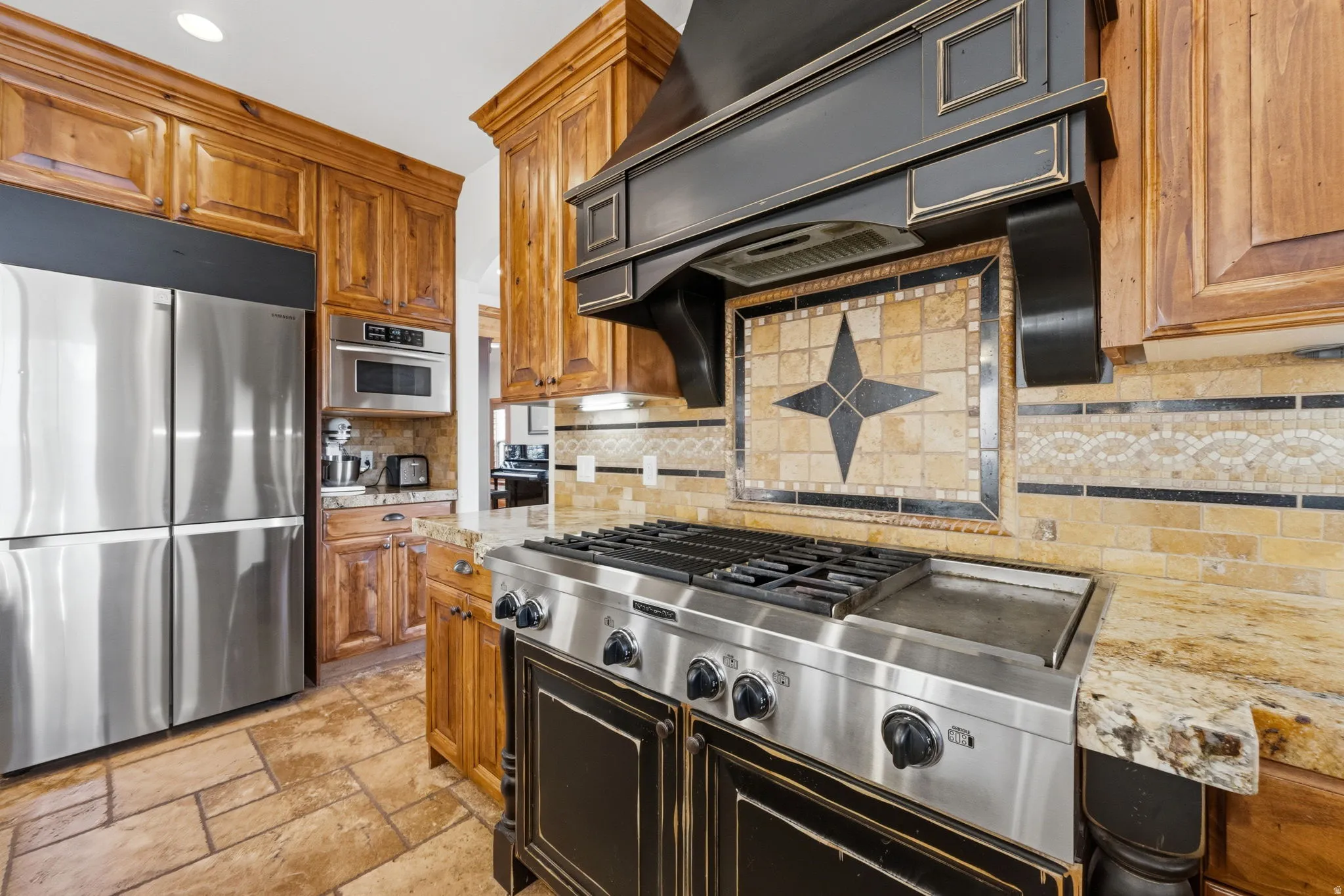 Kitchen with stainless steel appliances, light stone countertops, backsplash, stone tile flooring, and wood finish cabinets