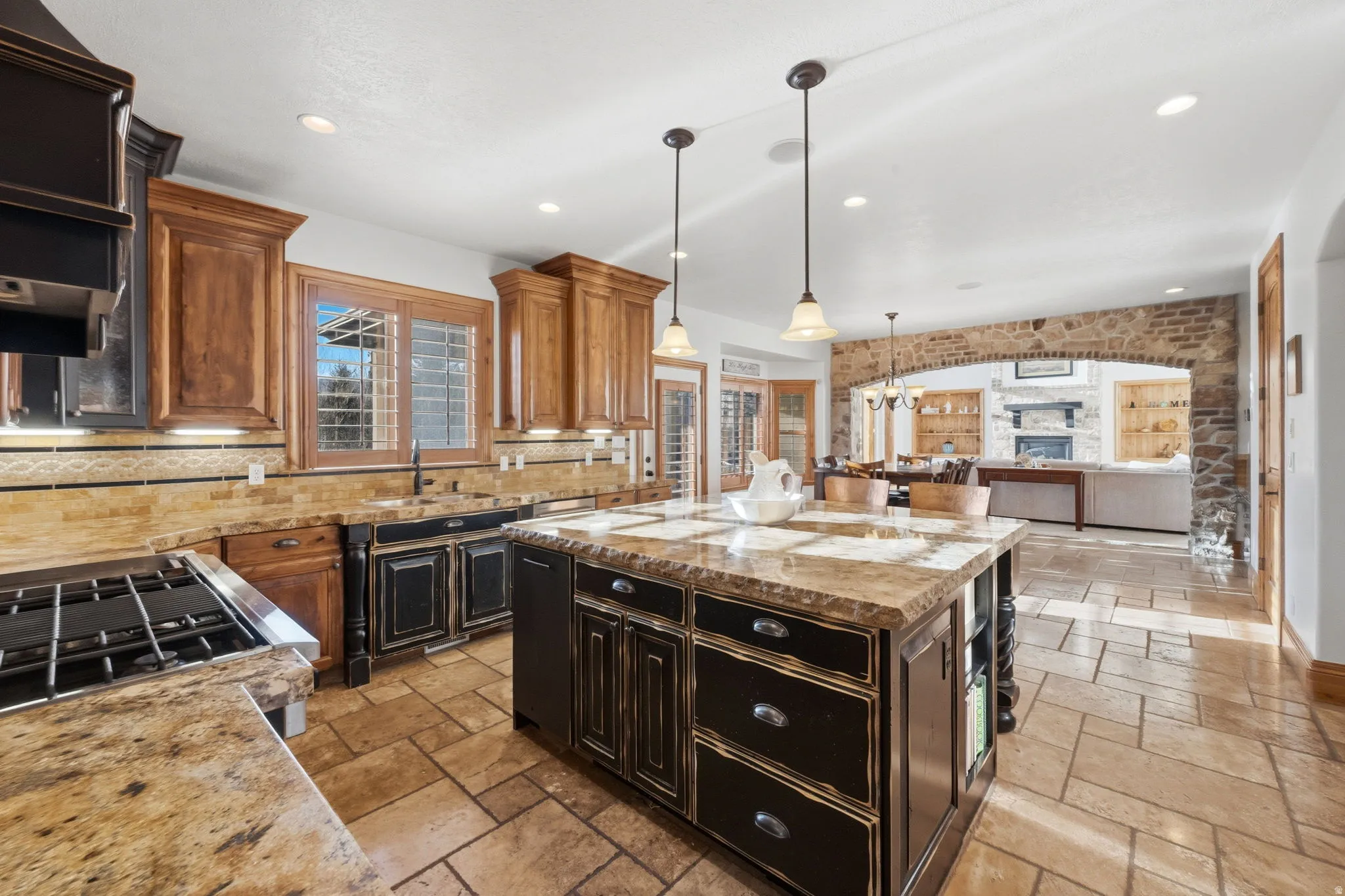 Dual tone kitchen with a center island, light stone counters, open floor plan, hanging light fixtures, and stone tile flooring