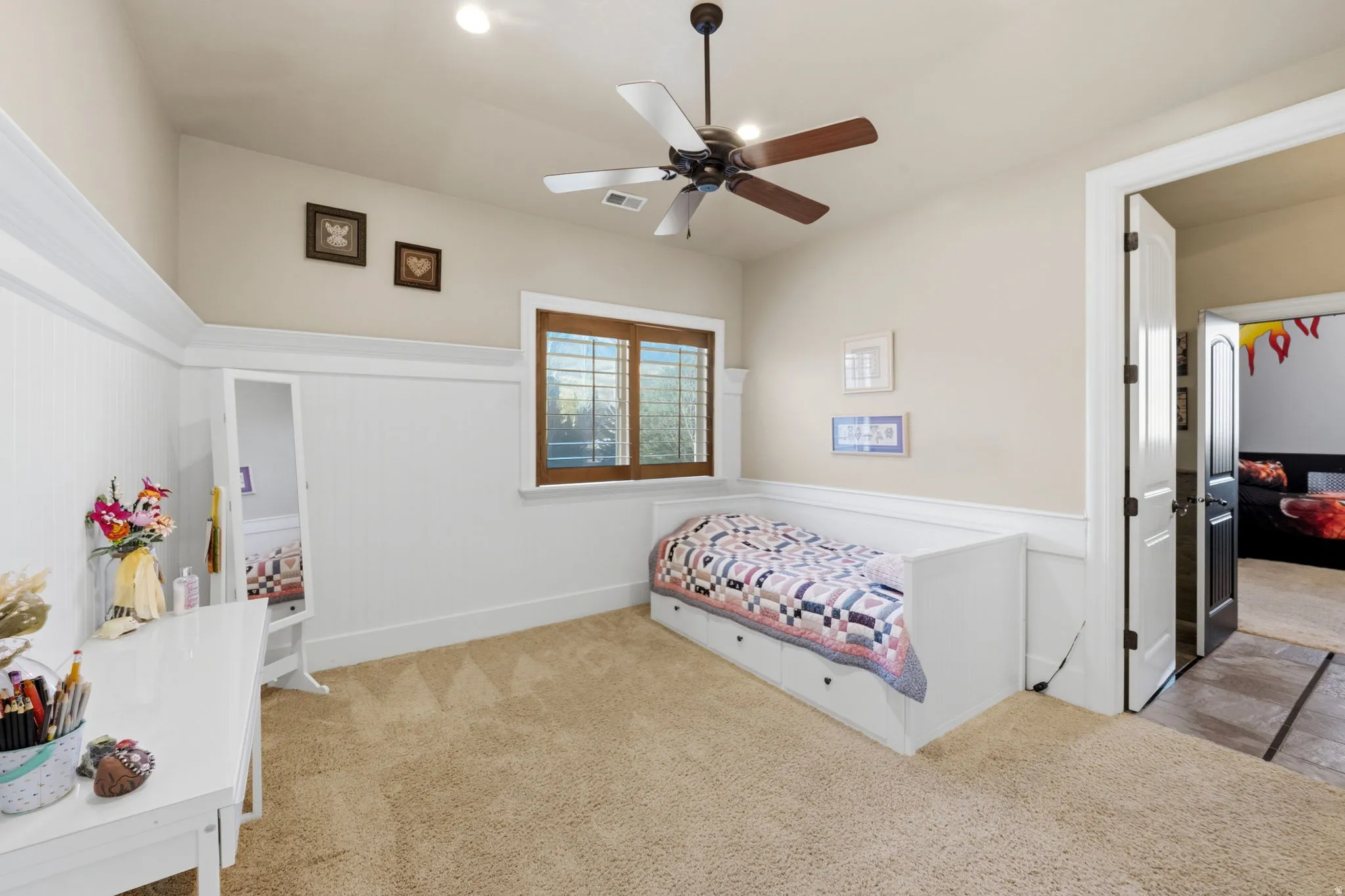 Bedroom featuring a wainscoted wall, light colored carpet, a decorative wall, and ceiling fan