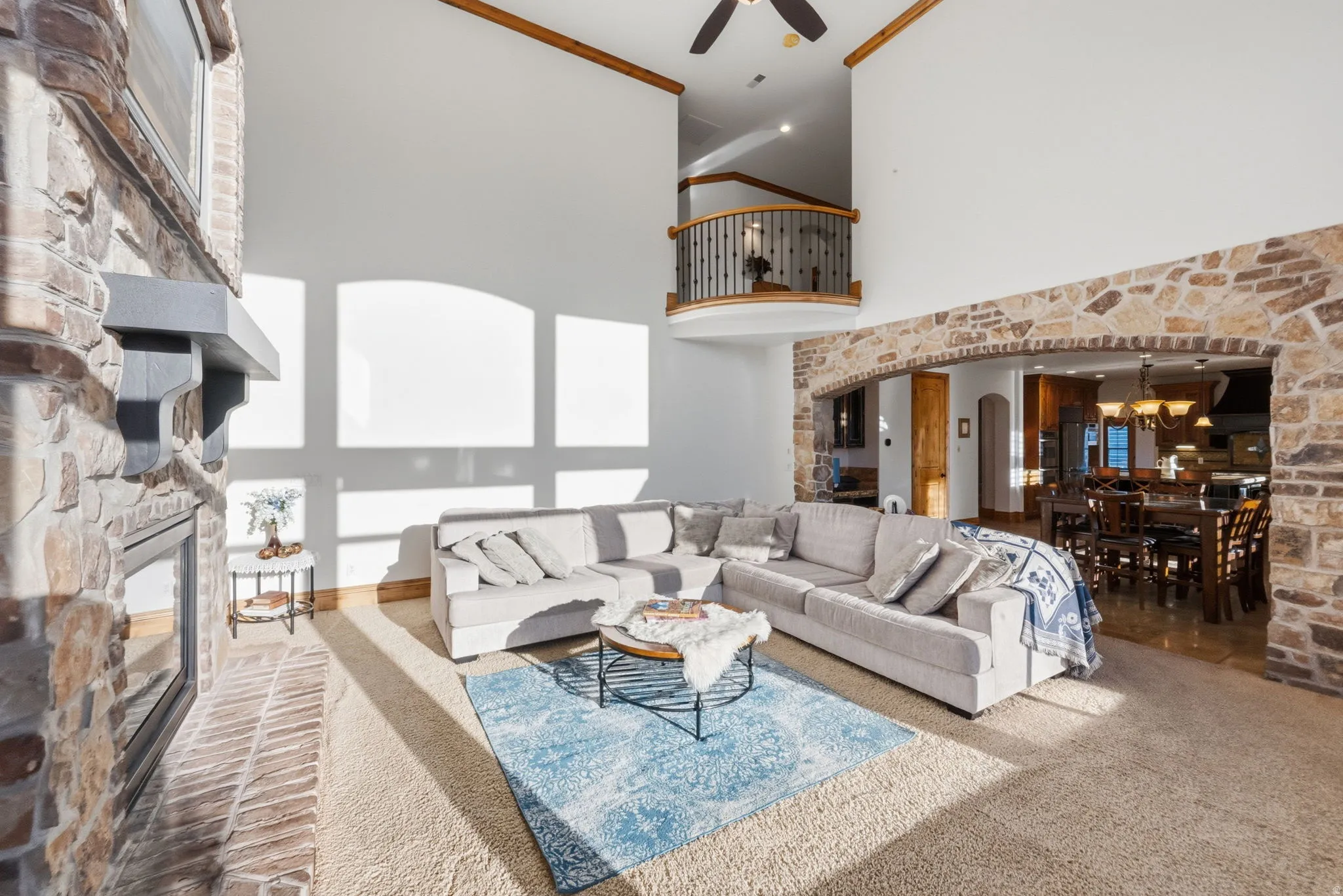 Carpeted living room featuring a fireplace, arched walkways, a high ceiling, a ceiling fan, and a chandelier