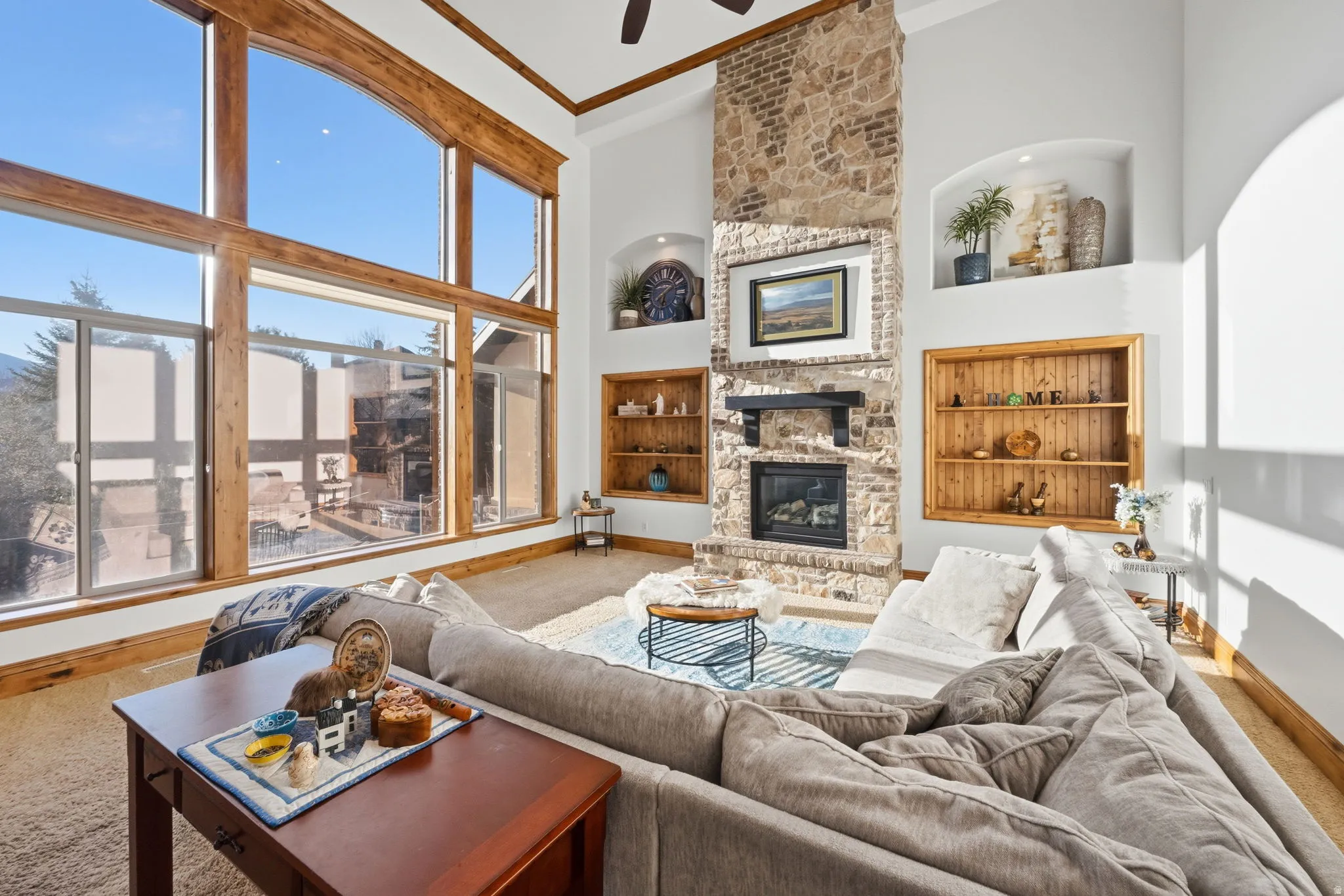 Carpeted living room featuring built in shelves, a fireplace, ornamental molding, a high ceiling, and ceiling fan