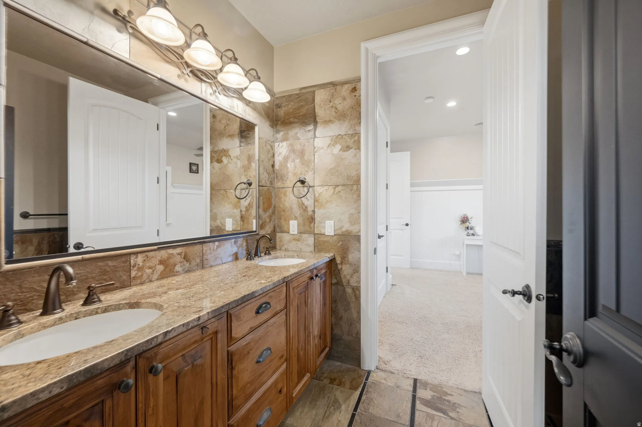 Bathroom featuring stone tile flooring, double vanity, wainscoting, and recessed lighting