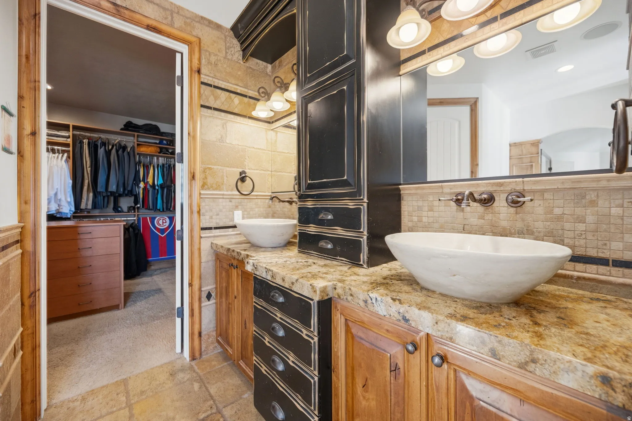 Full bathroom featuring double vanity, a walk in closet, stone tile flooring, recessed lighting, and decorative backsplash