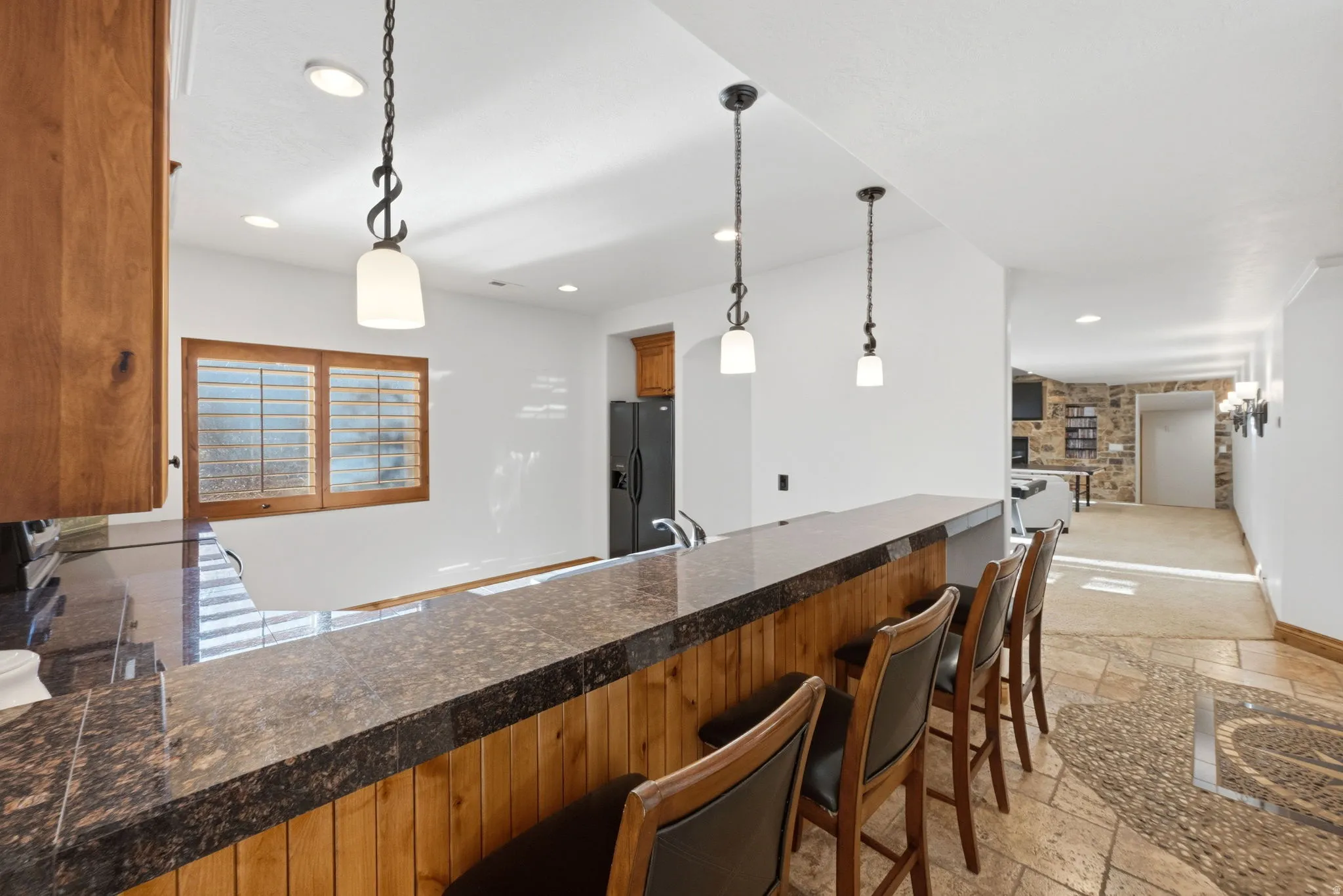 Kitchen featuring dark countertops, hanging light fixtures, stone tile floors, black fridge, and wood finish cabinetry