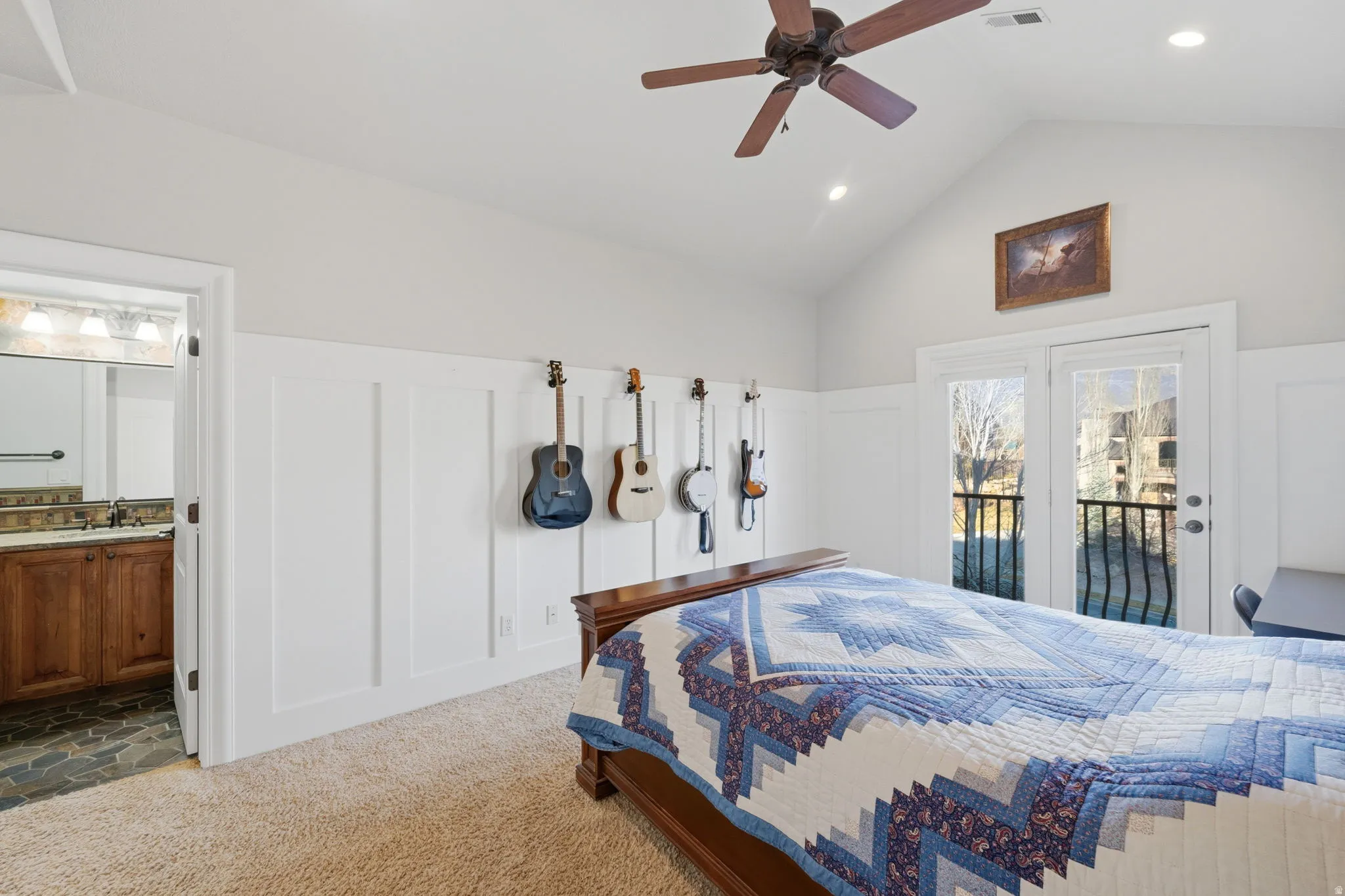 Bedroom featuring a decorative wall, access to exterior, vaulted ceiling, wainscoting, and ceiling fan