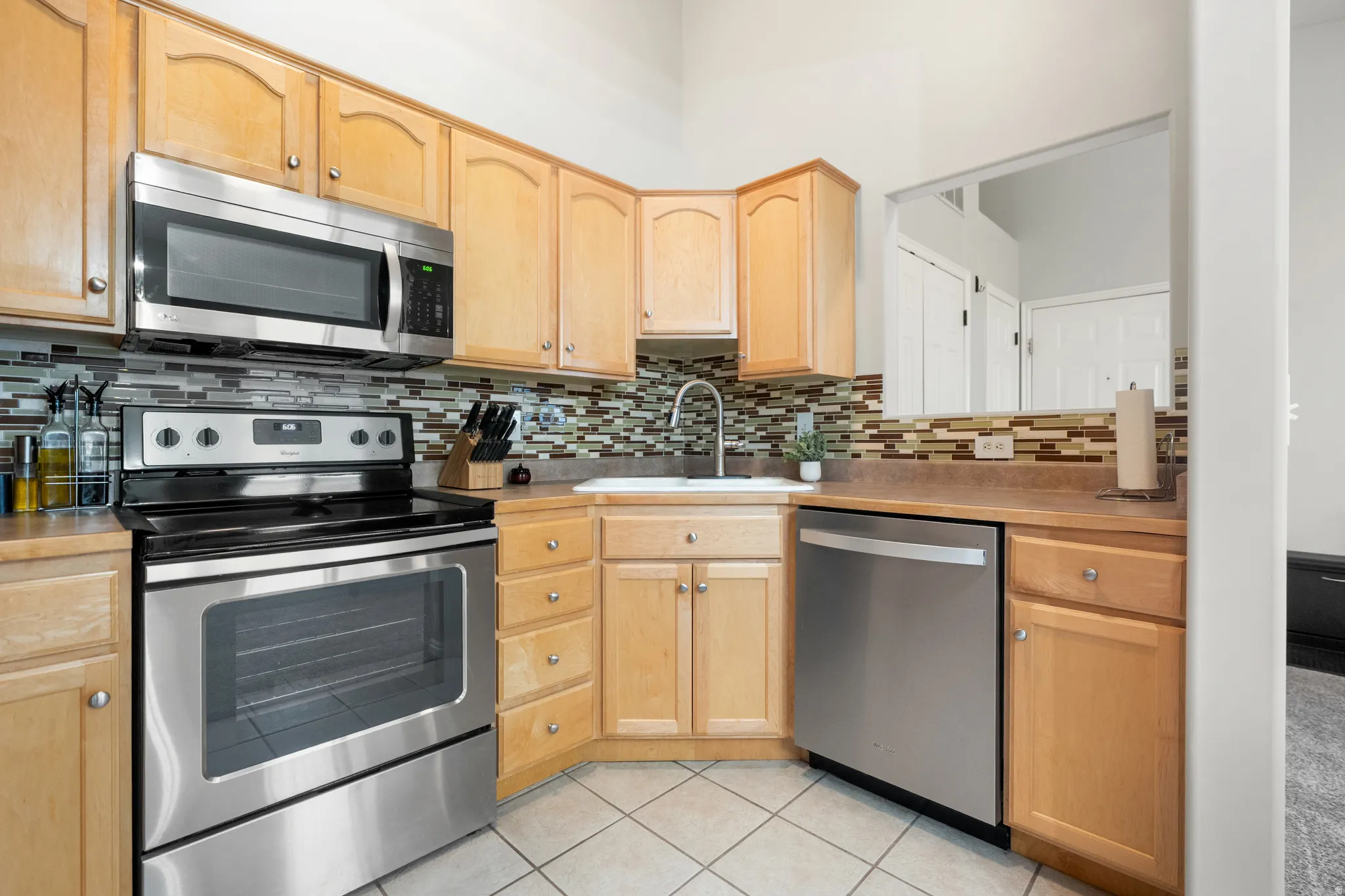 Kitchen featuring stainless steel appliances, light wood finish cabinets, backsplash, light countertops, and light tile patterned floors