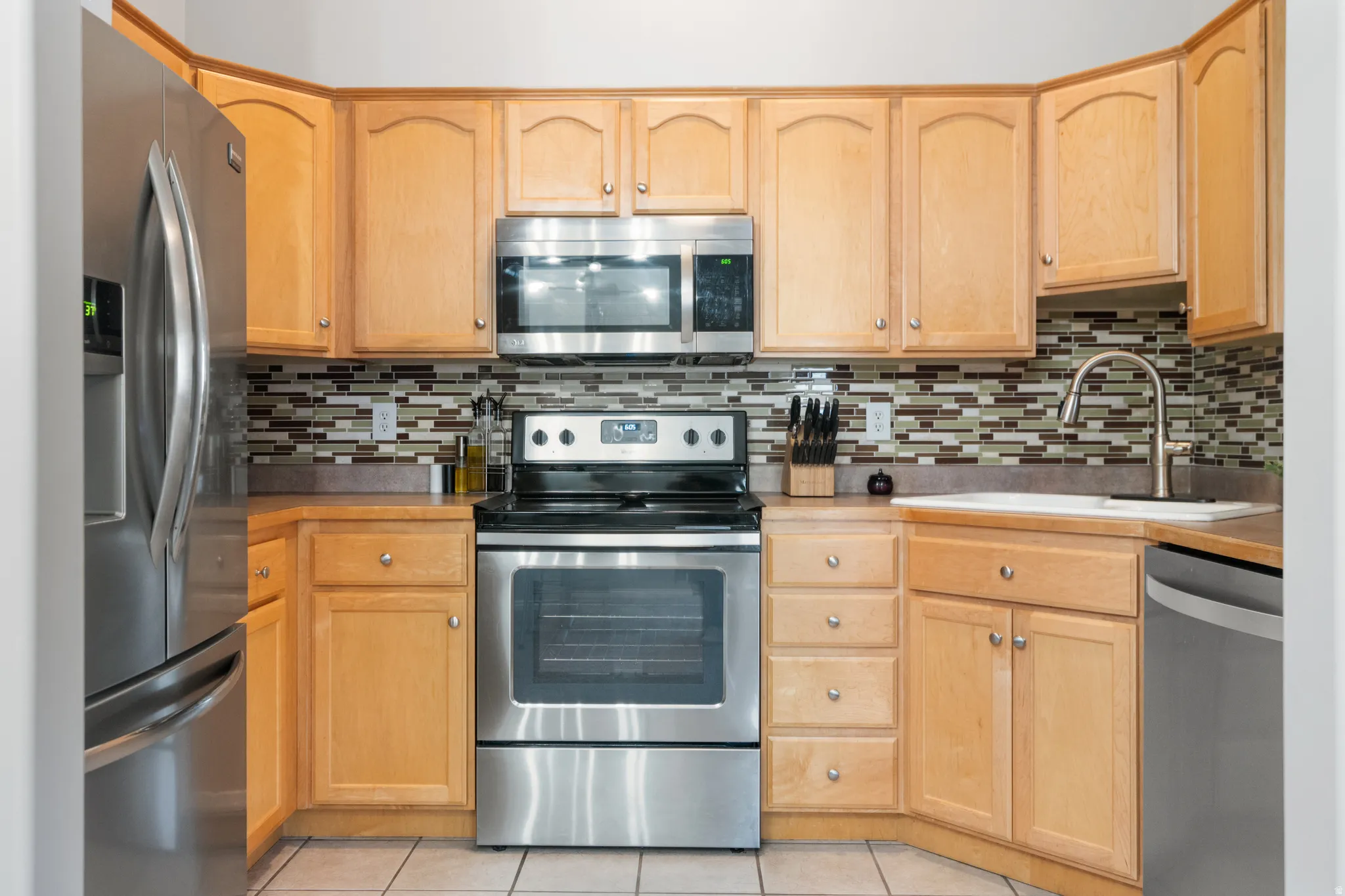 Kitchen with stainless steel appliances, light wood finish cabinetry, and light tile patterned floors