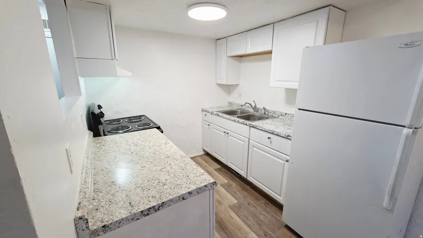 Kitchen with freestanding refrigerator, dark wood-style flooring, white cabinets, light countertops, and black electric range oven