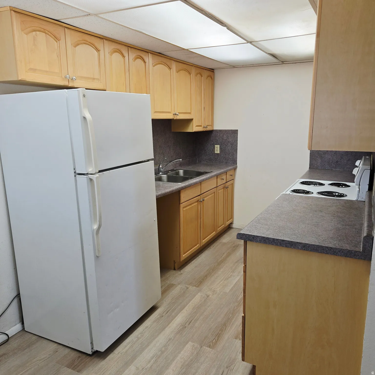 Kitchen featuring white appliances, light wood-type flooring, light wood finish cabinetry, dark countertops, and backsplash
