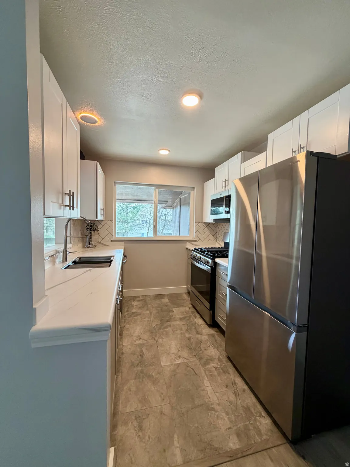Kitchen with stainless steel appliances, white cabinetry, tasteful backsplash, light stone countertops, and recessed lighting