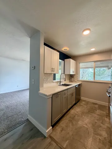 Kitchen with a textured ceiling, backsplash, white cabinets, dishwasher, and gray cabinets