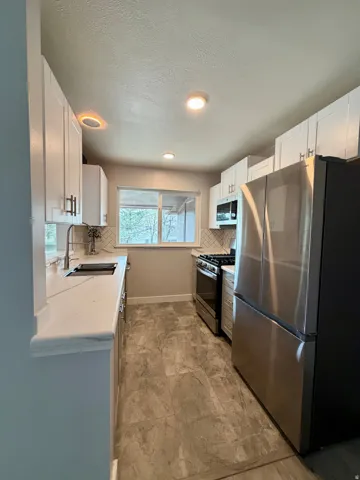 Kitchen with stainless steel appliances, white cabinetry, tasteful backsplash, light stone countertops, and recessed lighting
