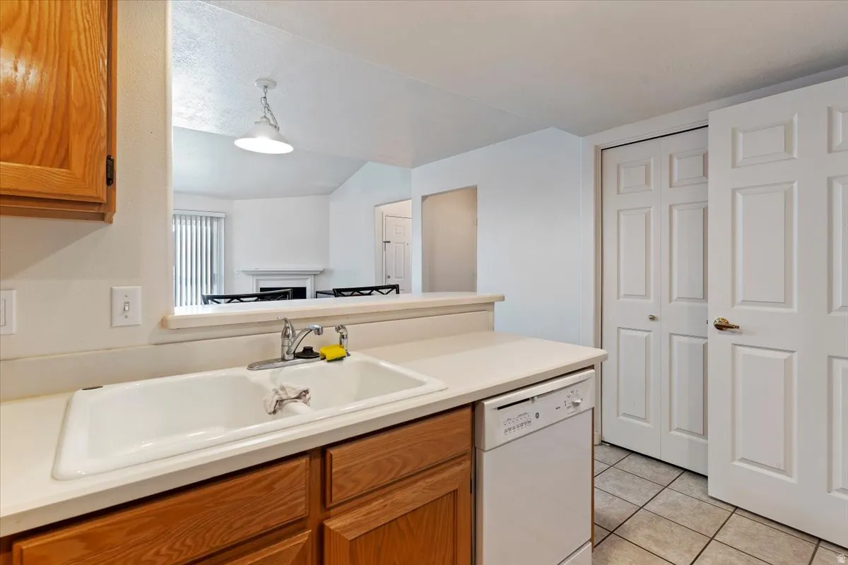 Kitchen featuring wood finish cabinets, light countertops, white dishwasher, and light tile patterned floors