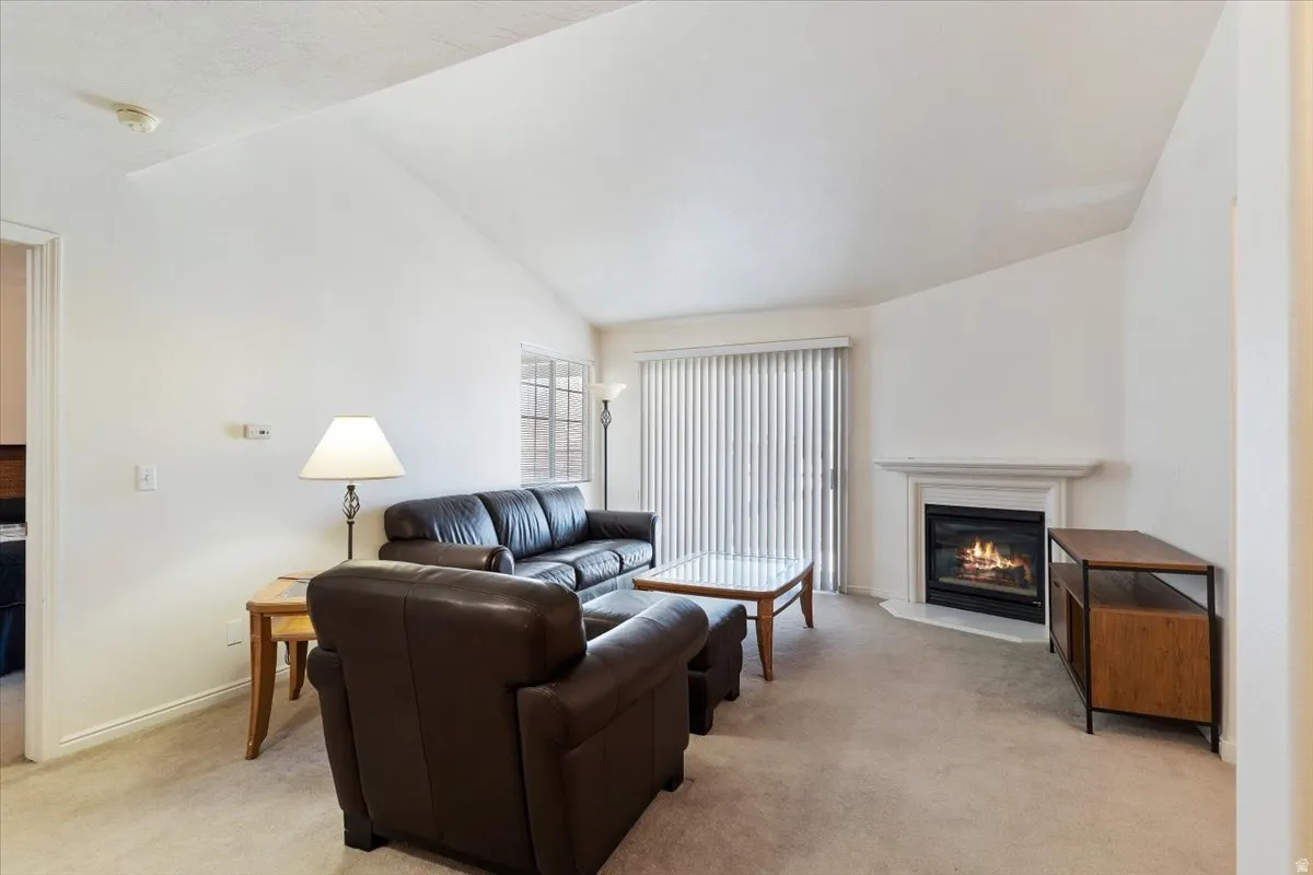 Living room with lofted ceiling, a glass covered fireplace, and light colored carpet