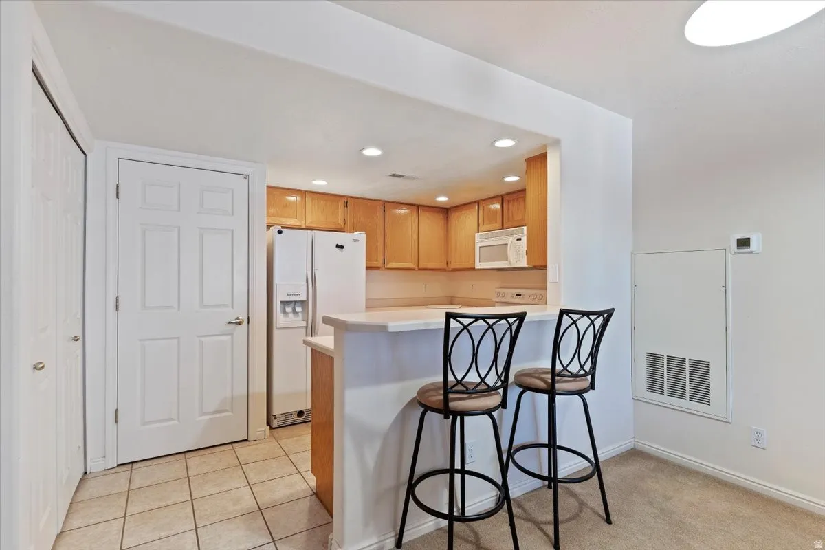 Kitchen with light countertops, white appliances, a kitchen bar, a peninsula, and recessed lighting