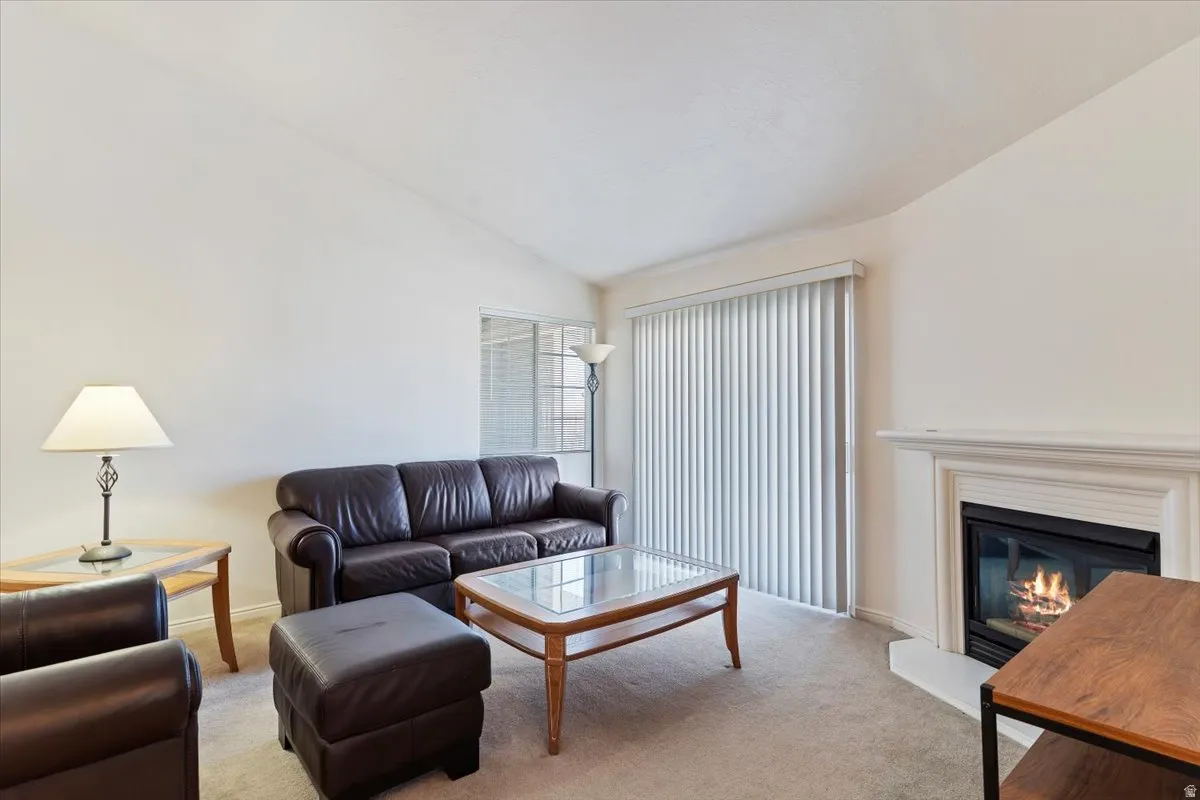 Living room with lofted ceiling, carpet floors, and a glass covered fireplace