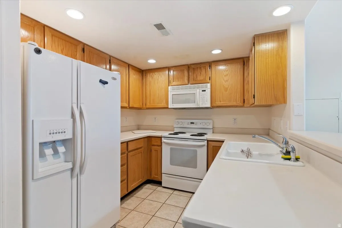 Kitchen with white appliances, light countertops, recessed lighting, light tile patterned flooring, and wood finish cabinets