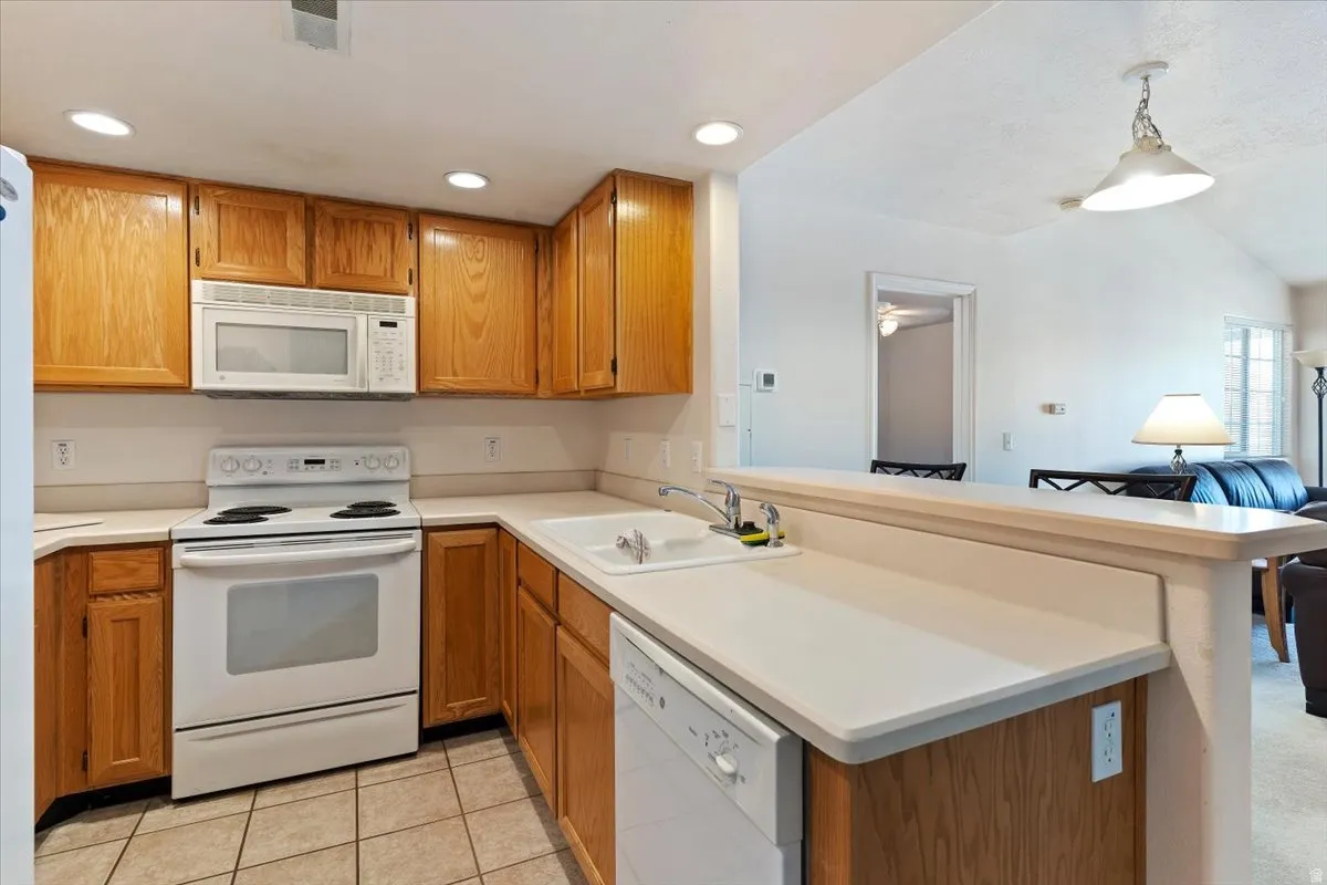 Kitchen featuring white appliances, light countertops, wood finish cabinetry, a peninsula, and light tile patterned floors