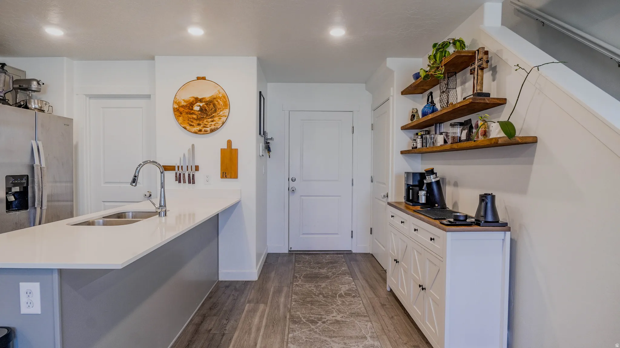 Kitchen featuring a peninsula, stainless steel refrigerator with ice dispenser, white cabinetry, dark wood-style floors, and light stone countertops