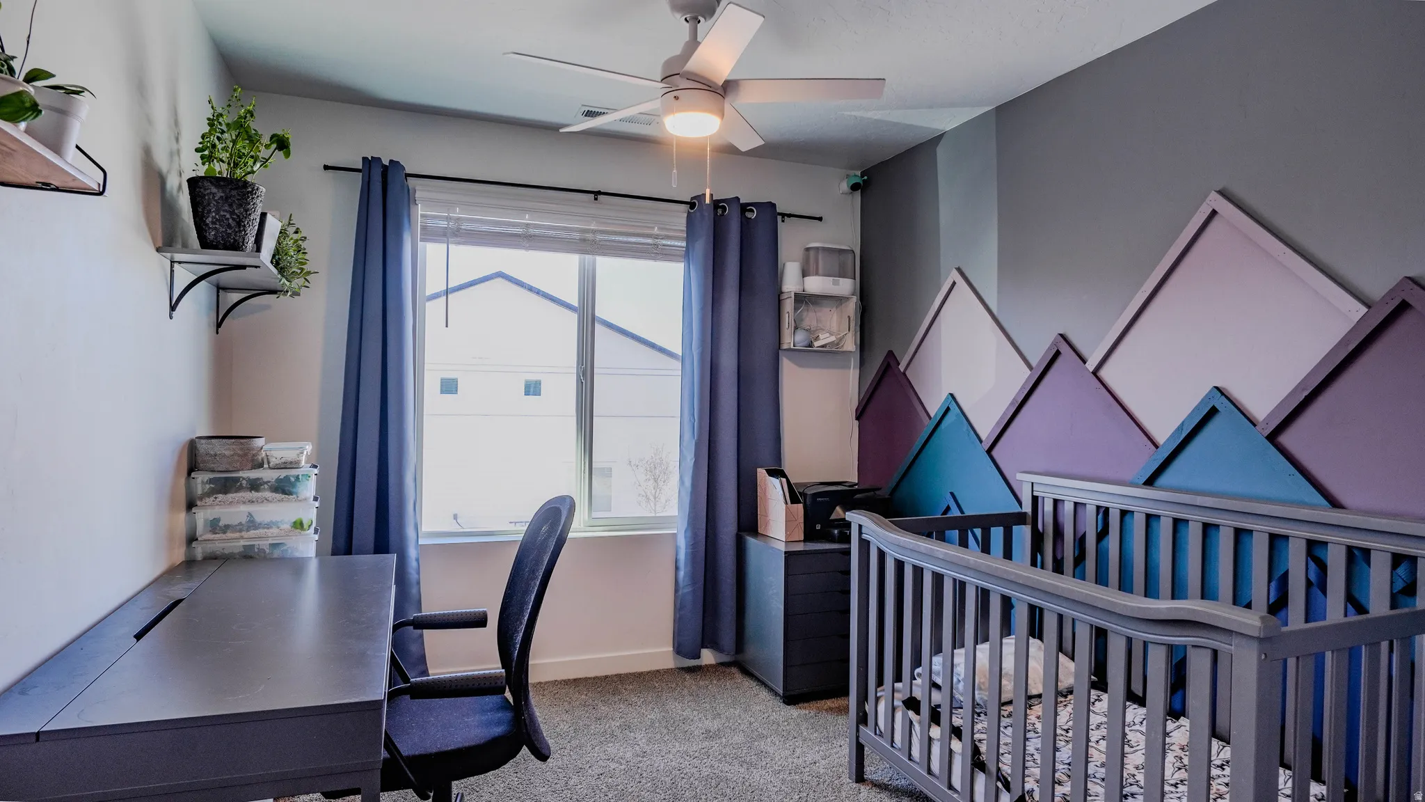Bedroom featuring a crib, ceiling fan, an office area, and light colored carpet
