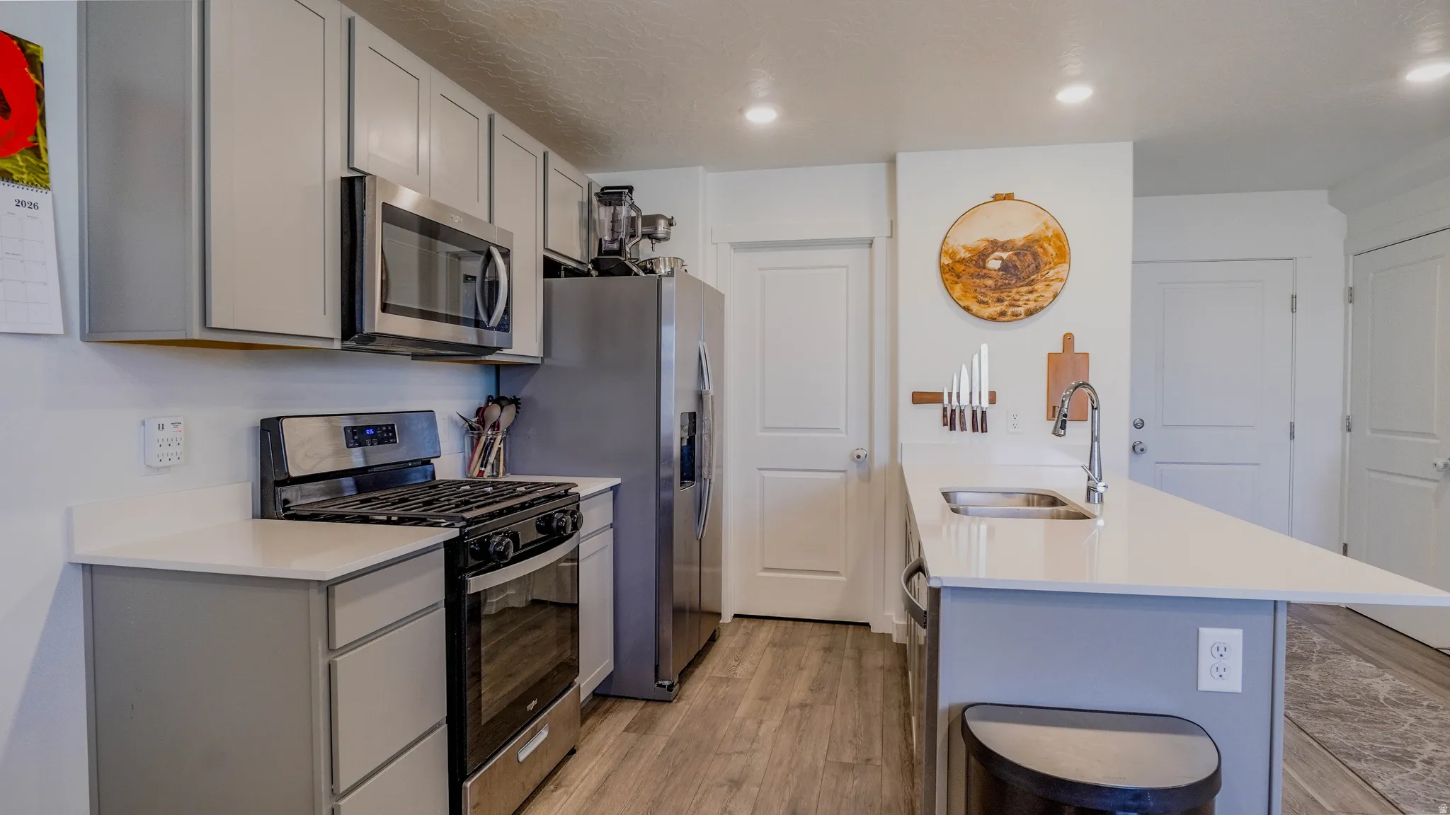 Kitchen with stainless steel appliances, gray cabinets, light wood-style flooring, light stone counters, and recessed lighting