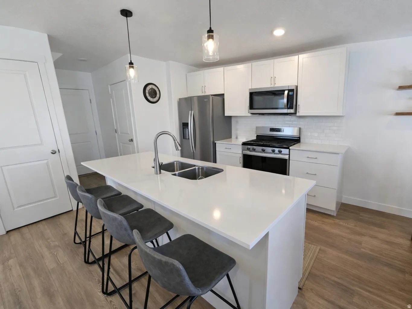 Kitchen featuring white cabinets, stainless steel appliances, a kitchen bar, a kitchen island with sink, and hanging light fixtures