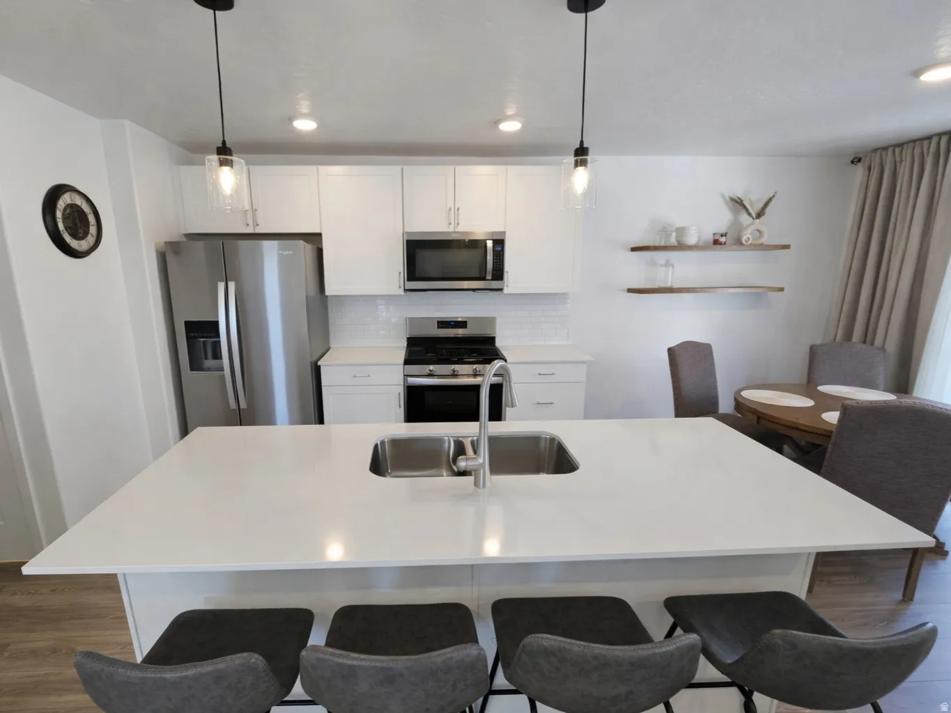 Kitchen with stainless steel appliances, white cabinetry, dark wood-style floors, and decorative light fixtures