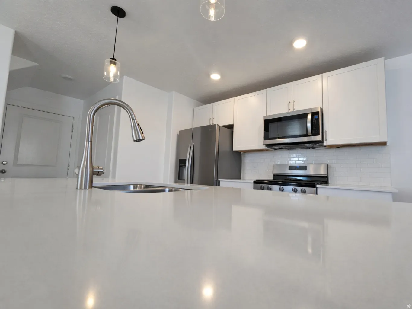 Kitchen featuring white cabinetry, stainless steel appliances, decorative backsplash, decorative light fixtures, and light stone countertops