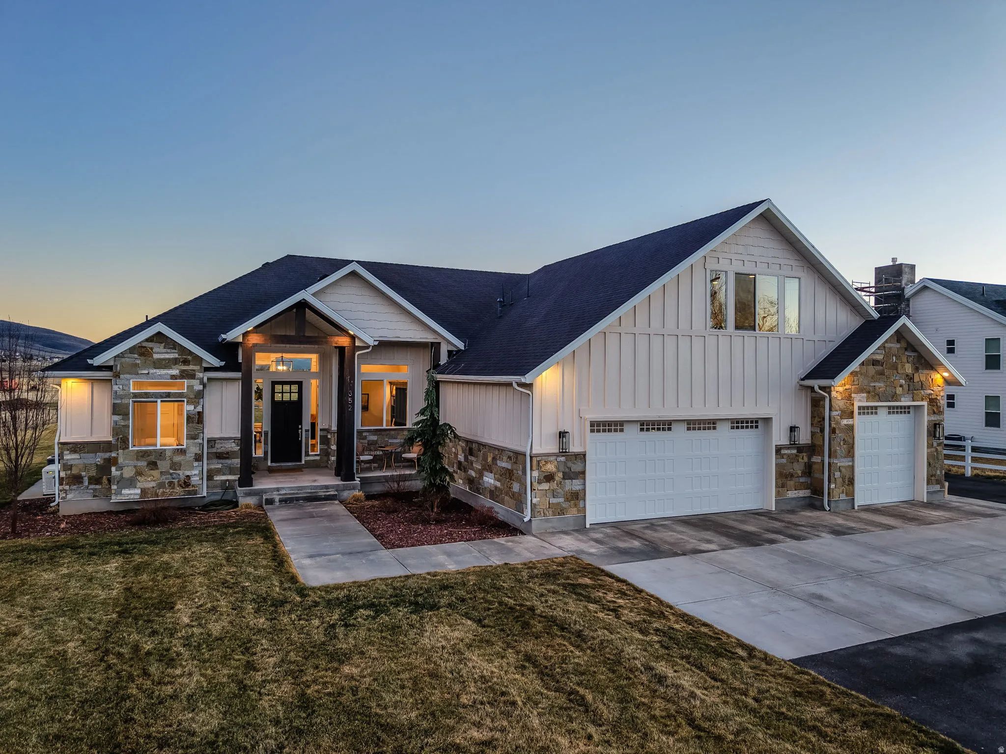 View of front of house featuring stone siding, board and batten siding, concrete driveway, a front lawn, and a garage