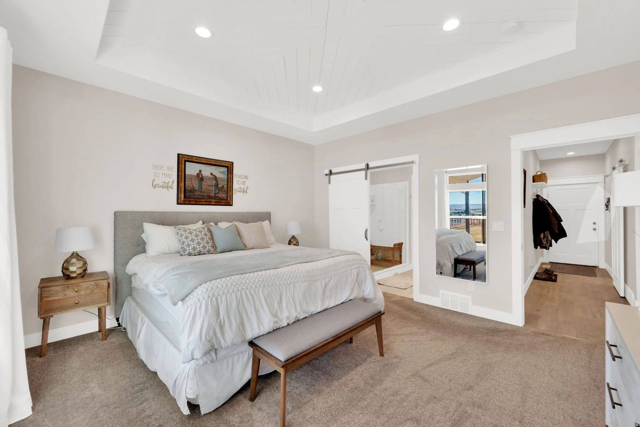 Carpeted bedroom featuring a barn door, recessed lighting, ensuite bathroom, and a tray ceiling