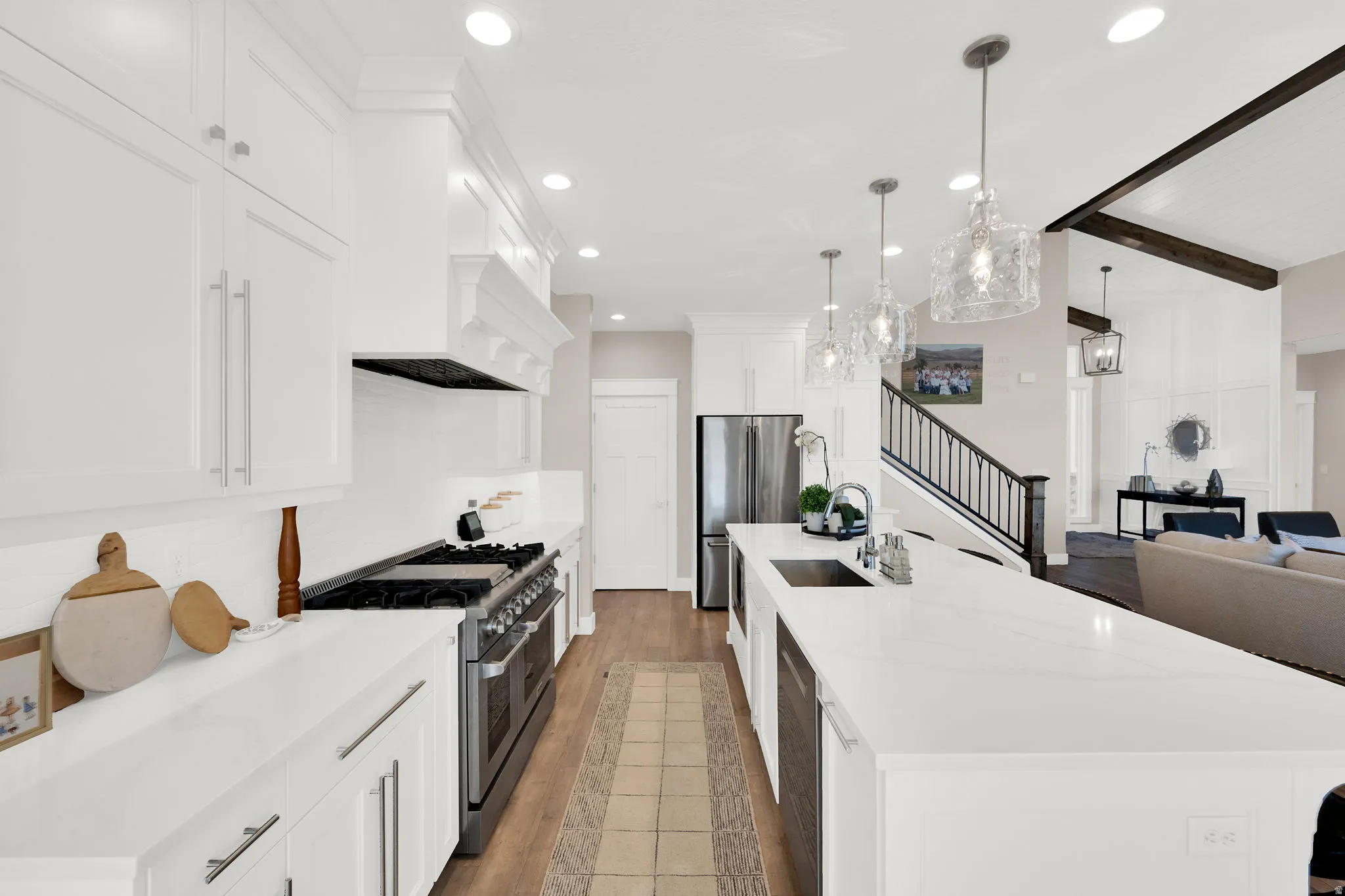 Kitchen featuring beam ceiling, light wood finished floors, stainless steel appliances, open floor plan, and a large island with sink