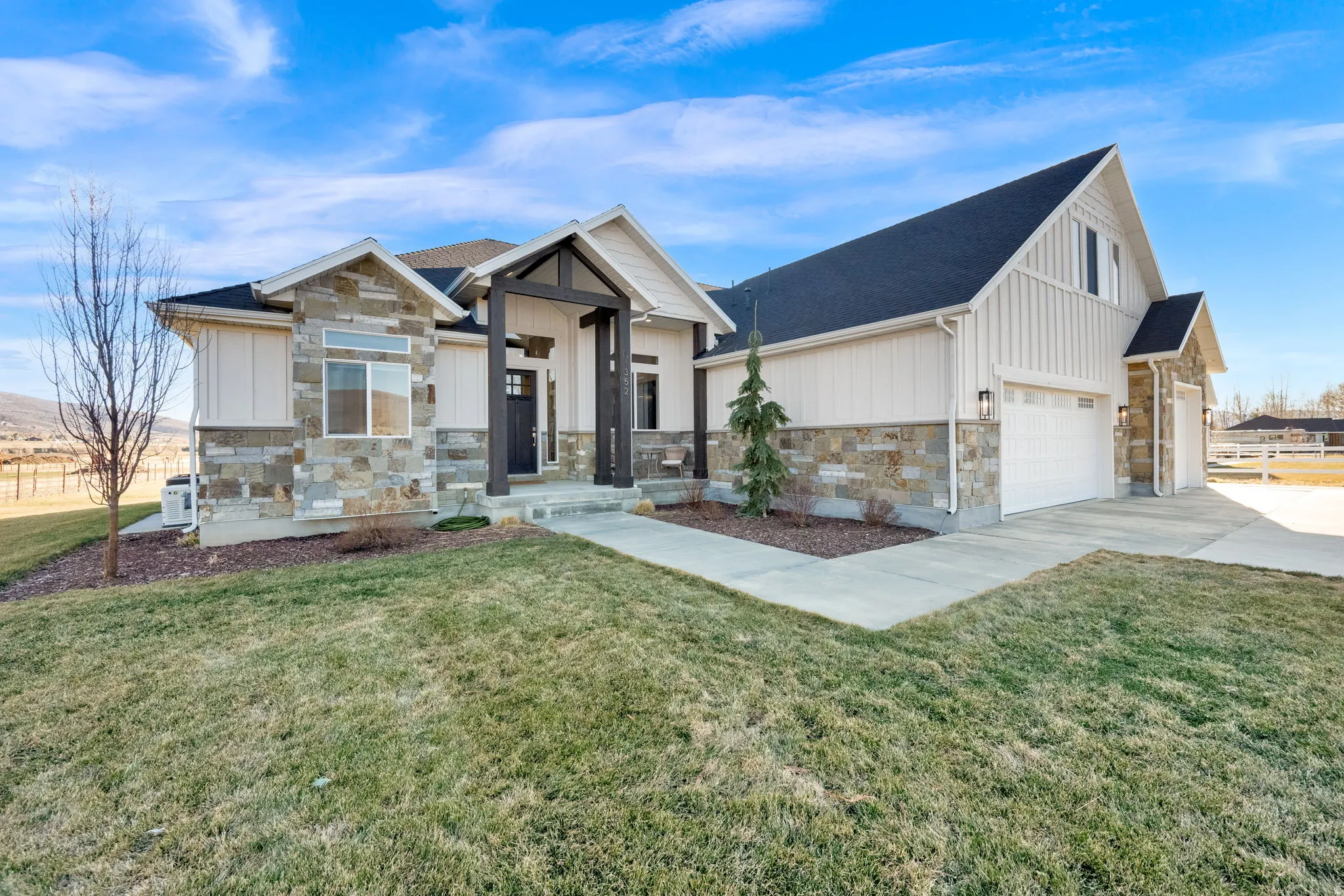 Modern farmhouse with stone siding, board and batten siding, a front yard, and concrete driveway