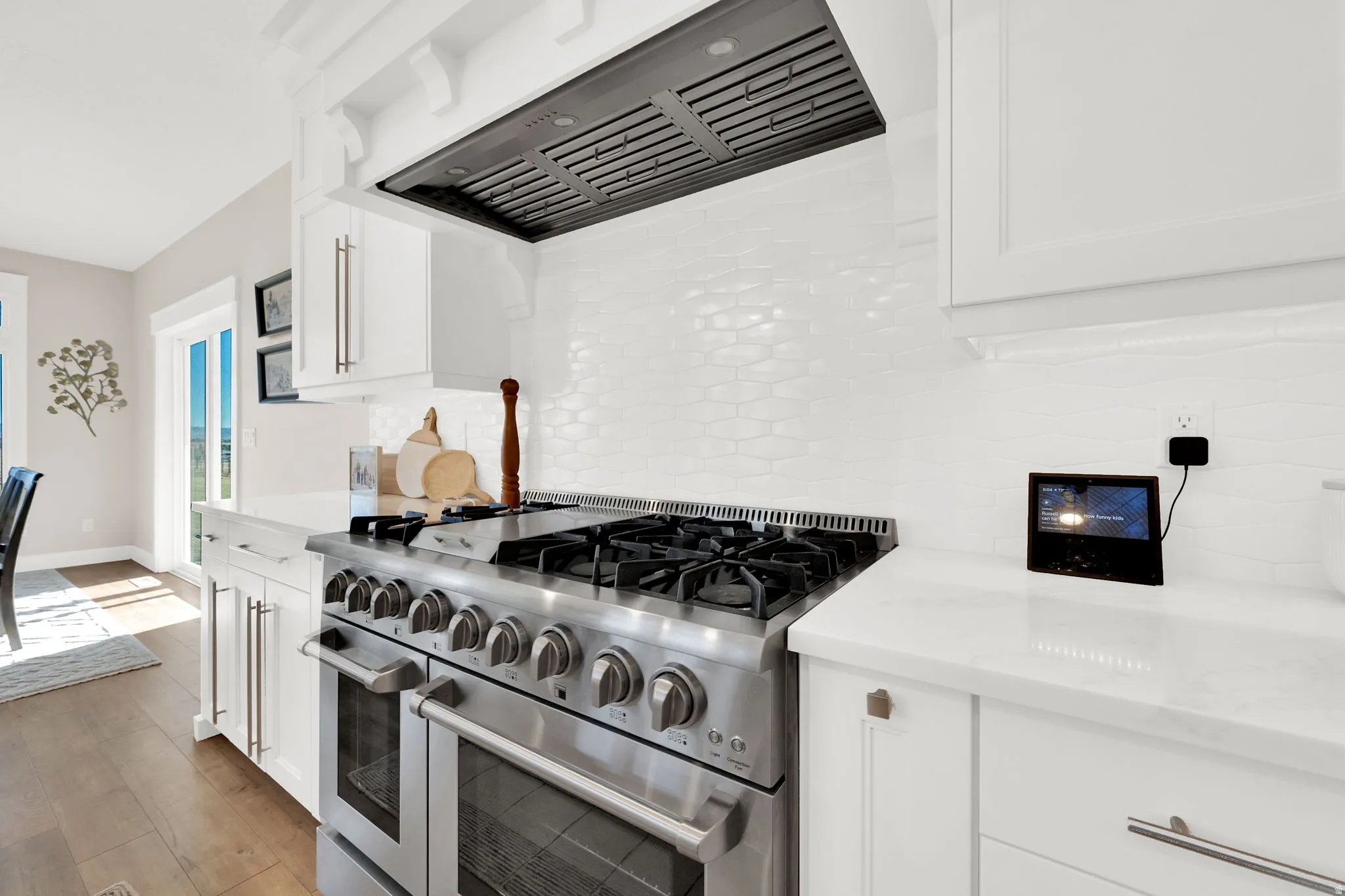 Kitchen featuring double oven range, white cabinetry, light stone counters, light wood-type flooring, and decorative backsplash