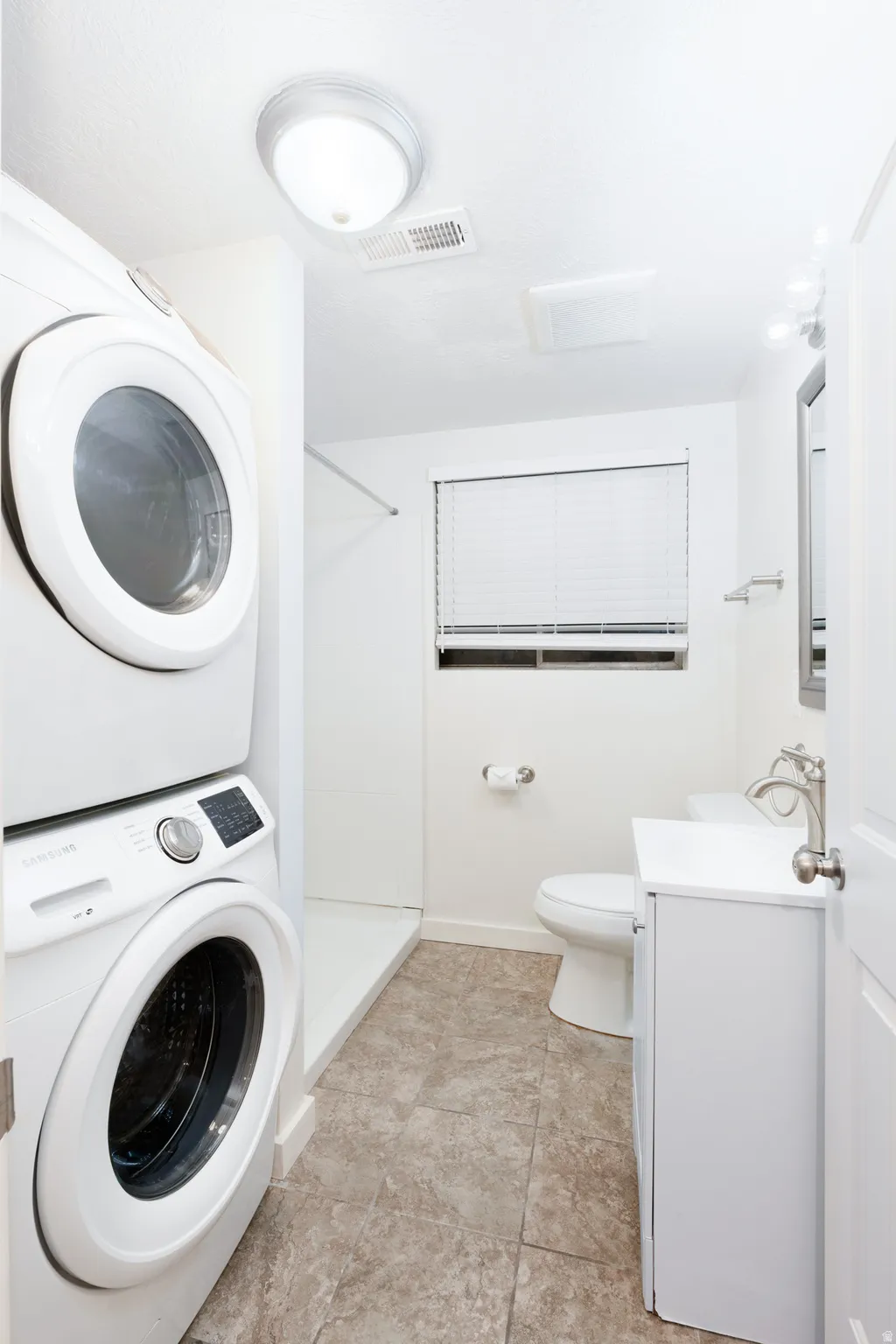Basement bathroom with a shower stall, vanity, and stacked washer and dryer.