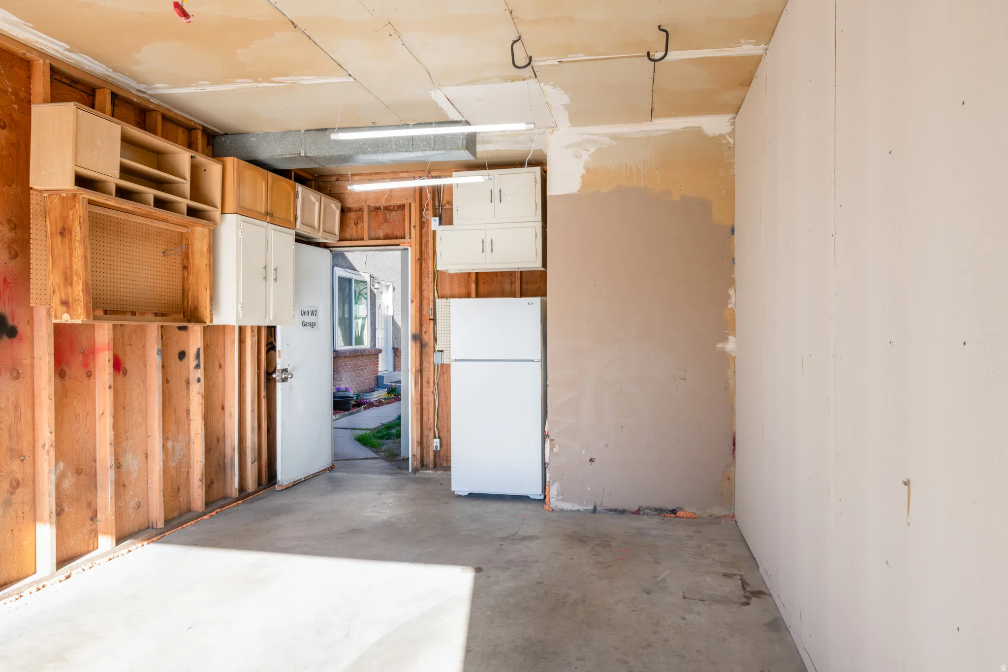 Single car garage featuring freestanding refrigerator and storage.