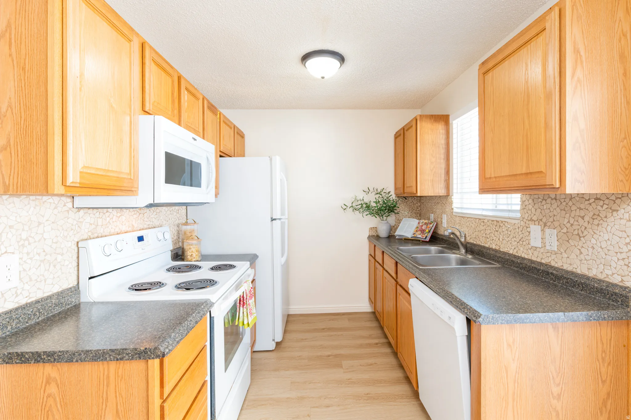 Kitchen featuring white appliances, backsplash, and dark countertops.